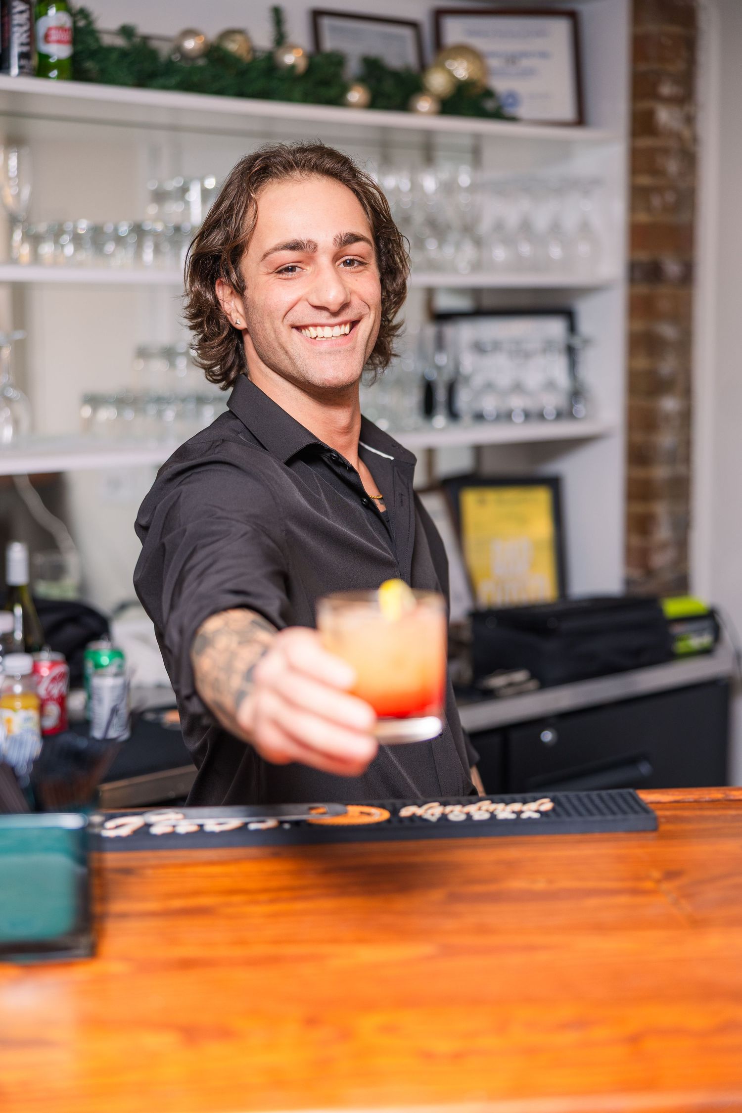Bartender behind wooden counter smiling while preparing drinks at an event.