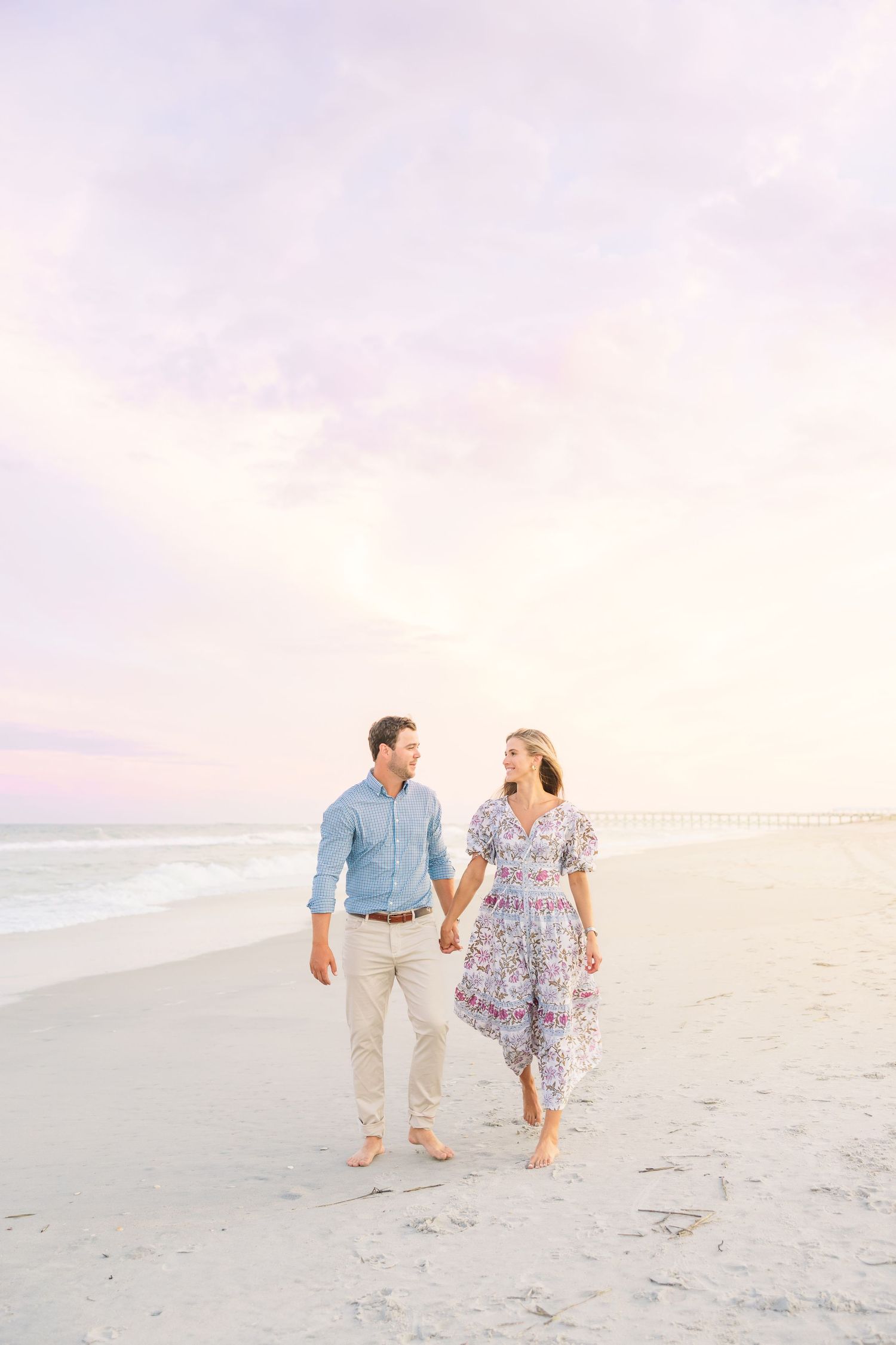 Couple walking barefoot together along empty beach during sunset.