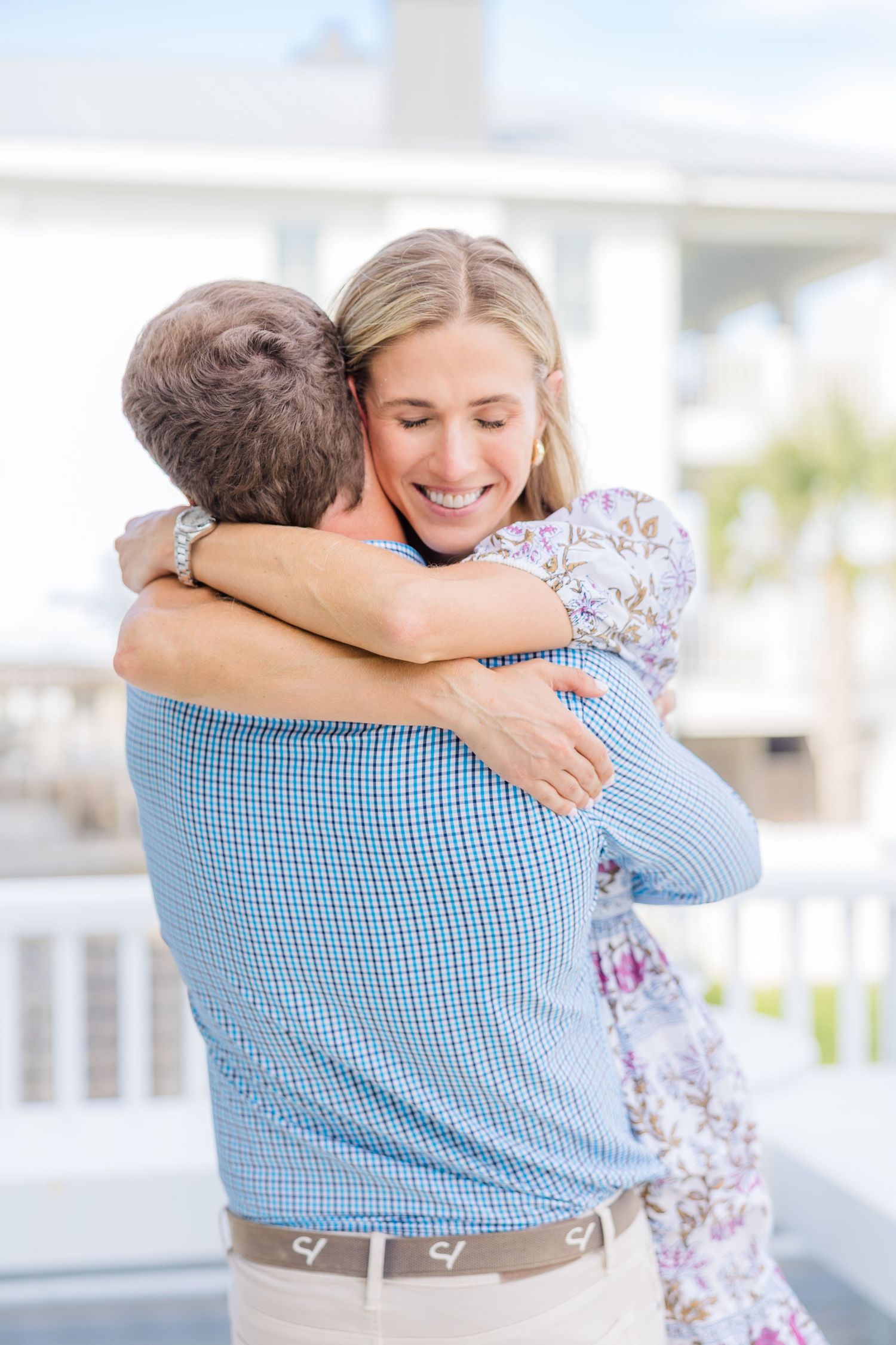 A couple embraces joyfully on a bright white porch during a celebration.