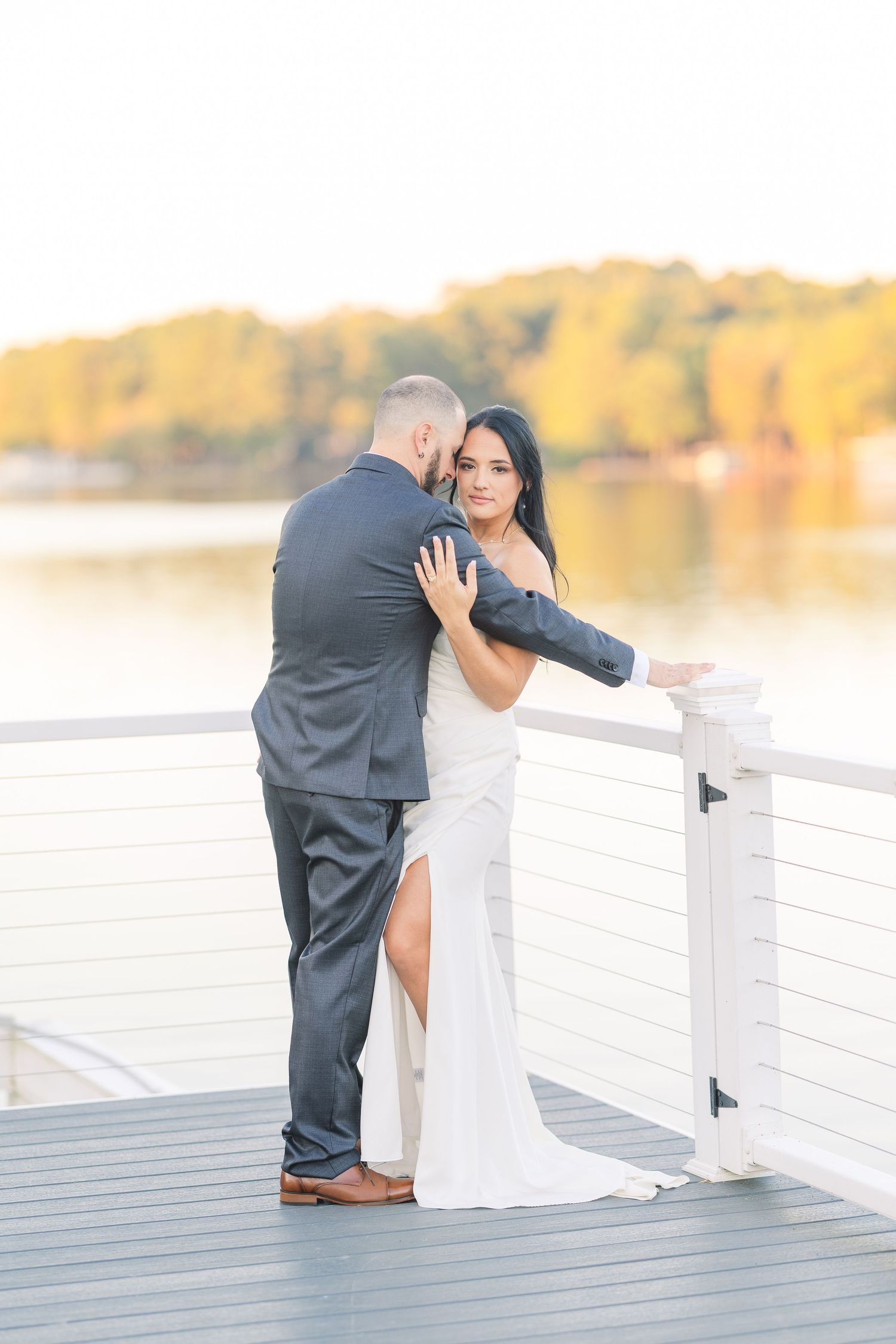 Sunset wedding photos on a lakeside dock with golden autumn colors in the background wedding groom bride lake Gaston photographer light airy