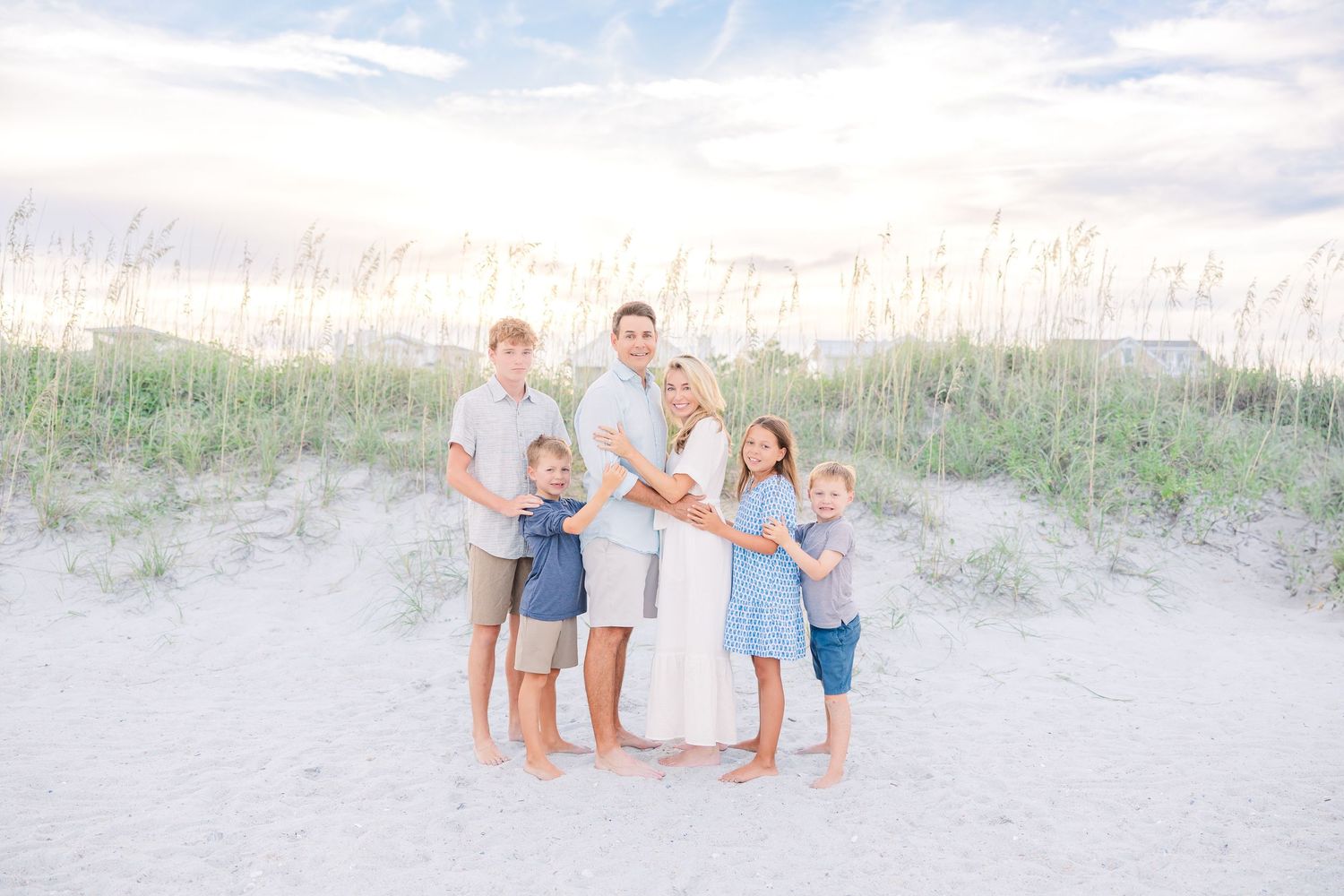 Family poses for casual portraits on sandy dunes with beach grass in background.