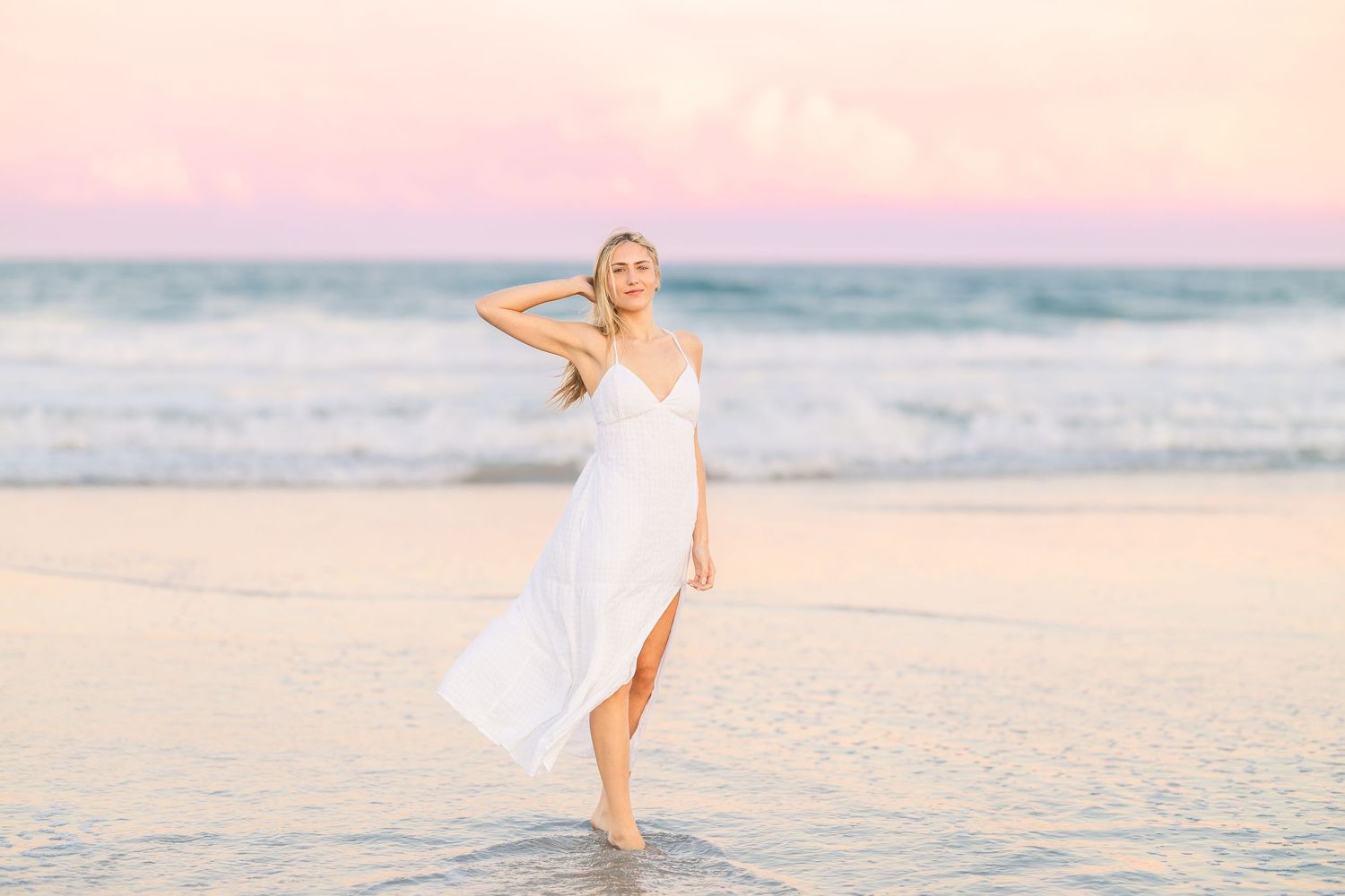 Carefree woman twirls in white dress on sandy beach during golden hour.