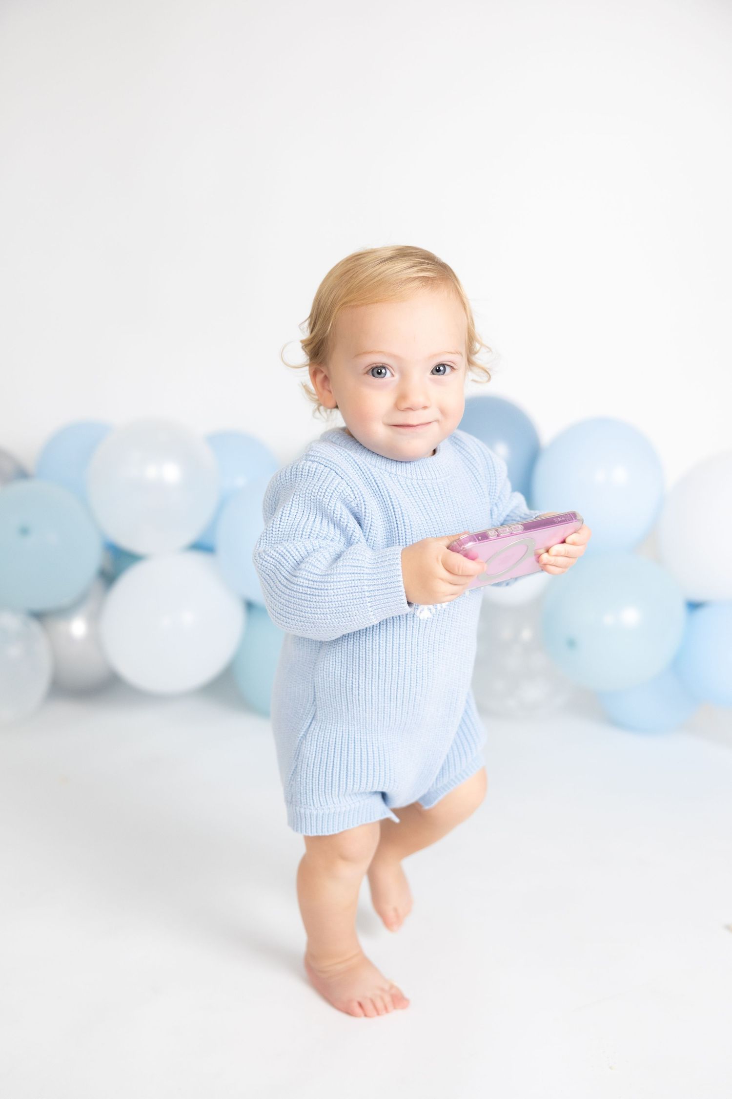 Baby wearing light blue sweater plays in front of pastel balloon decoration.