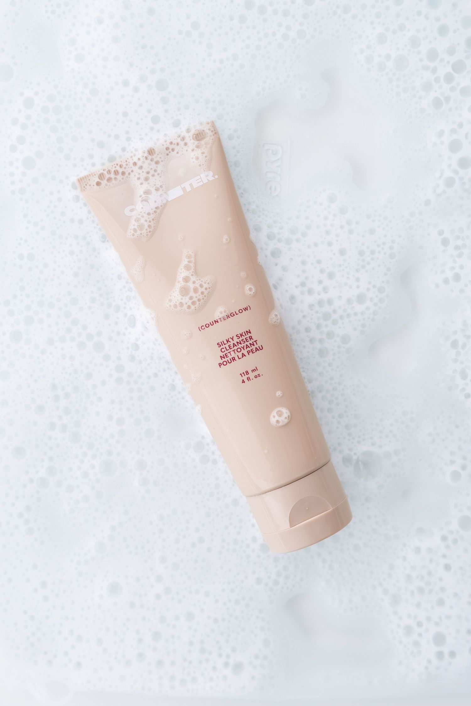 Beige cosmetic tube with foam texture on white background.