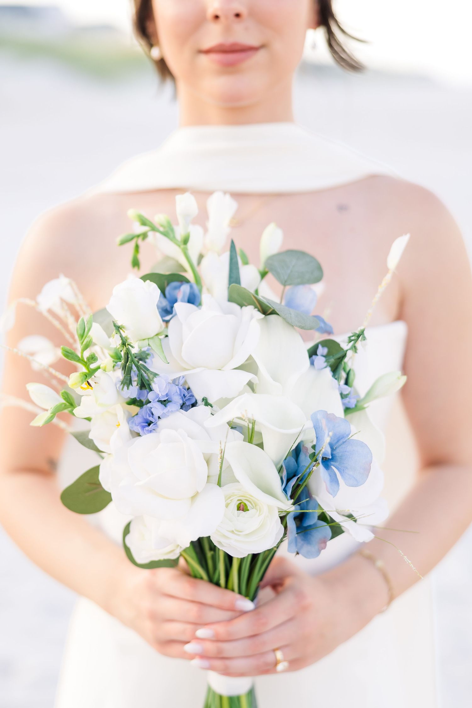 Bride holds a romantic bouquet of white roses and blue hydrangeas with eucalyptus greenery in Carolina Beach near Wilmington, NC.