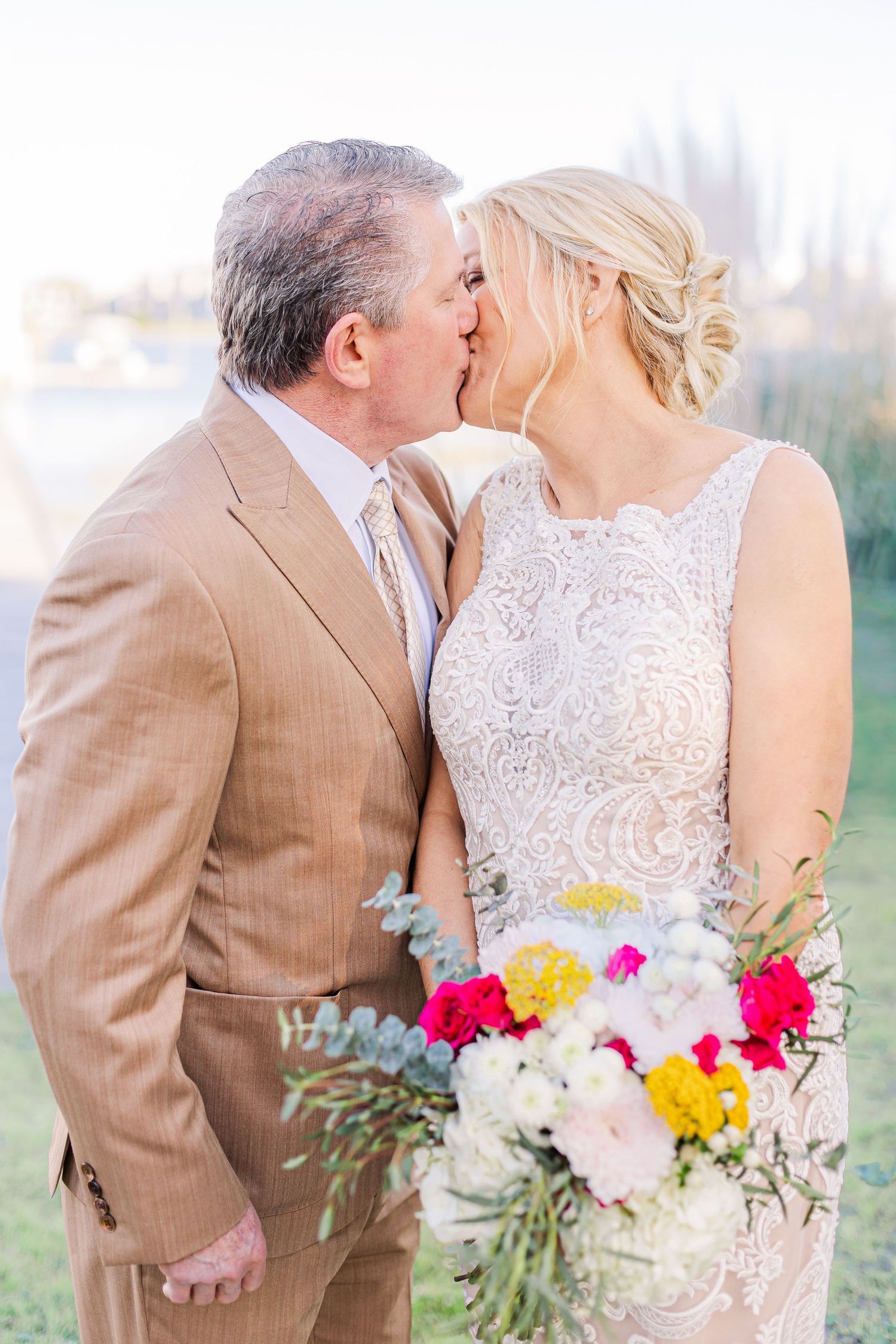 Couple embraces while holding vibrant bouquet with yellow and pink flowers.