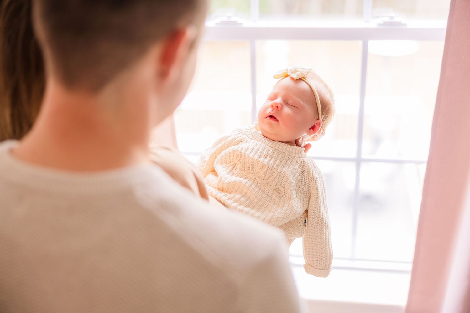 Gentle family moments captured in a bright sunlit room with delicate pink decor.