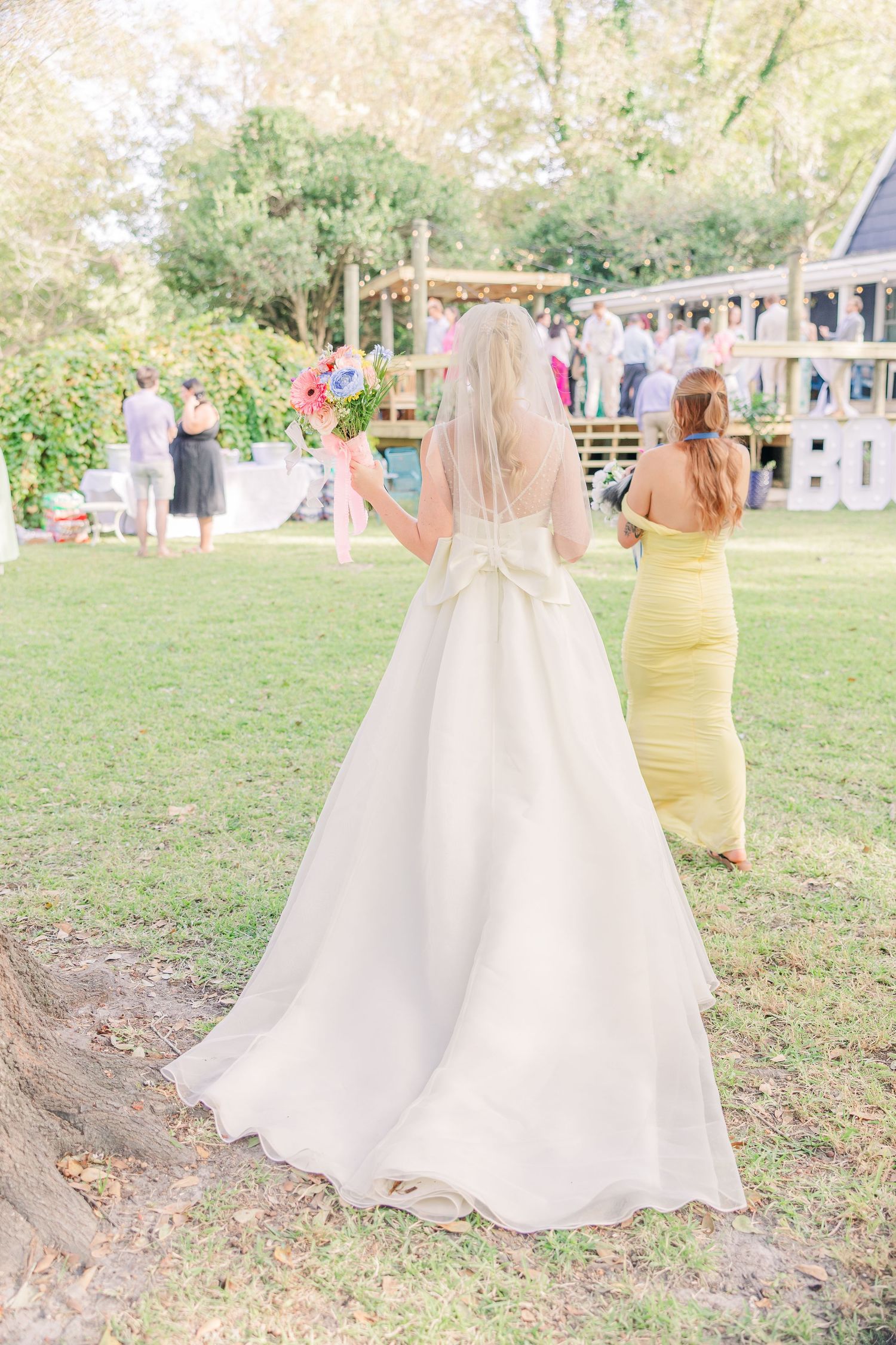 Elegant white wedding dress trains trail across green grass at outdoor ceremony.