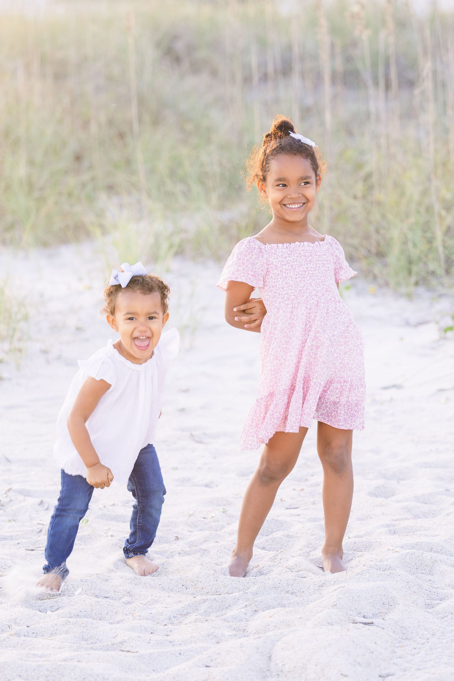 Two children in coordinated outfits play and laugh together on a sandy beach.