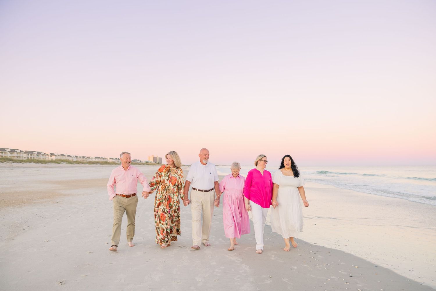 A group walks along a beach at sunset wearing coordinated pastel outfits.