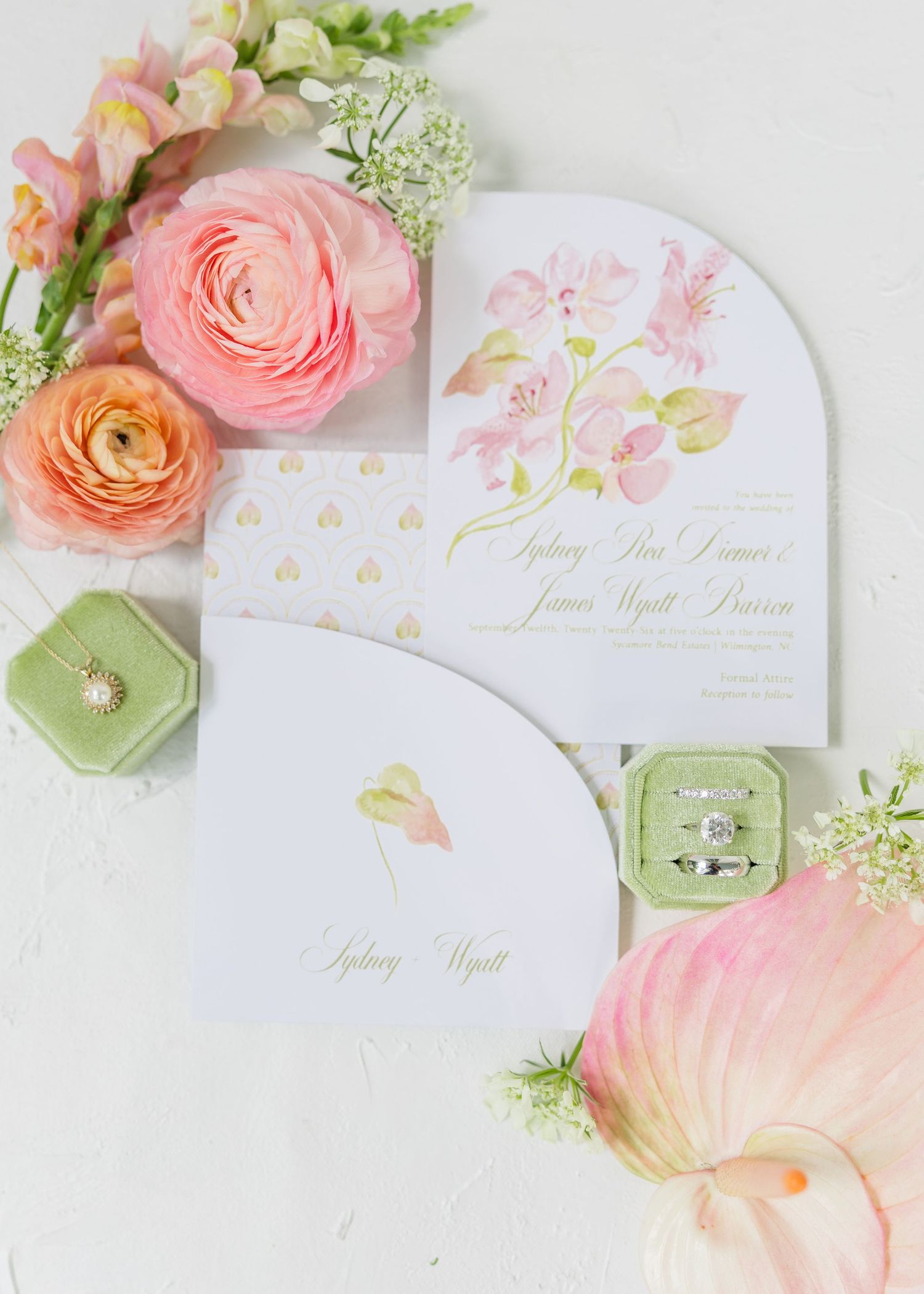 Elegant wedding invitation suite with floral watercolor design, diamond rings, and pink ranunculus flowers on white background.