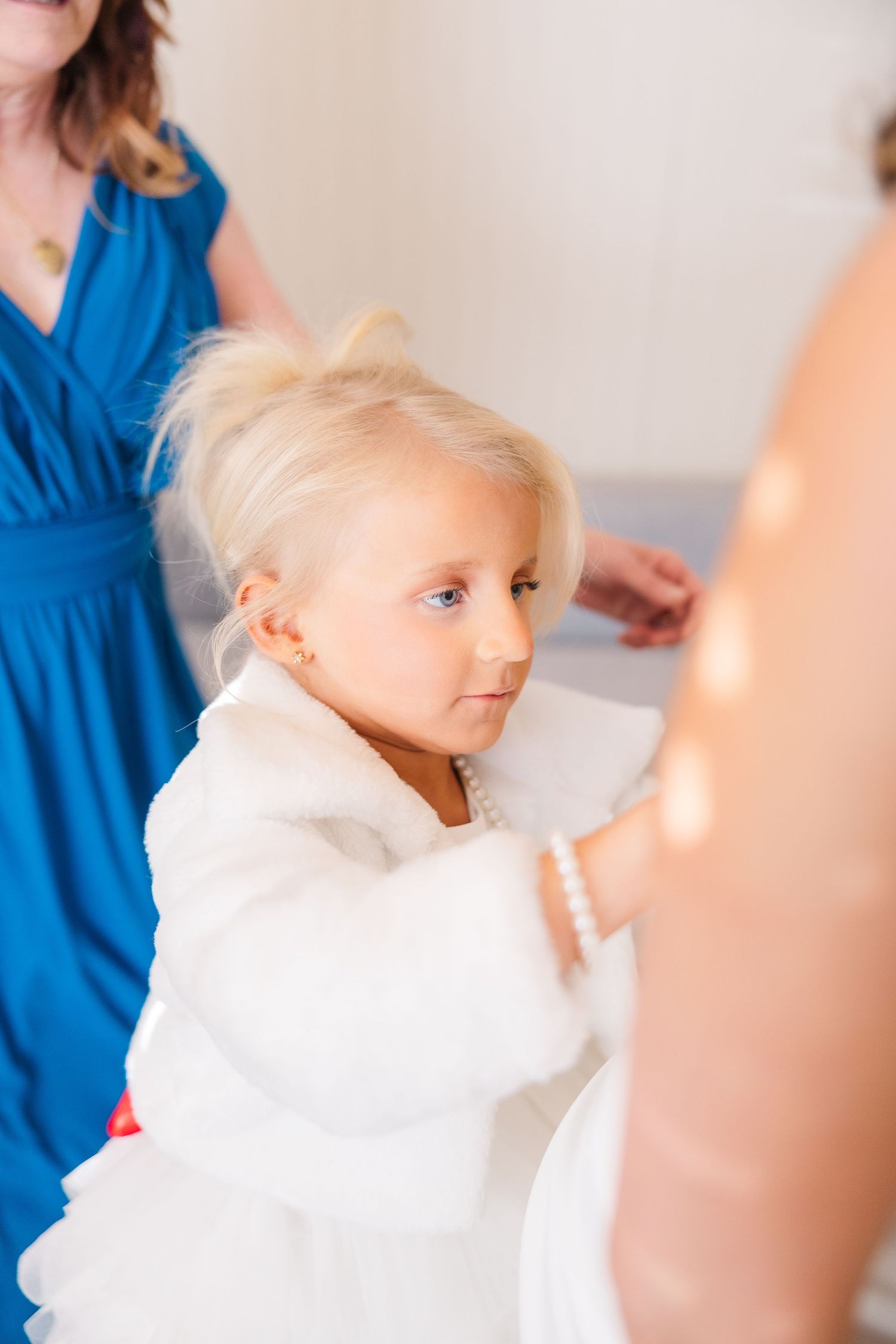 Young attendant in a white fuzzy jacket watching wedding preparations.