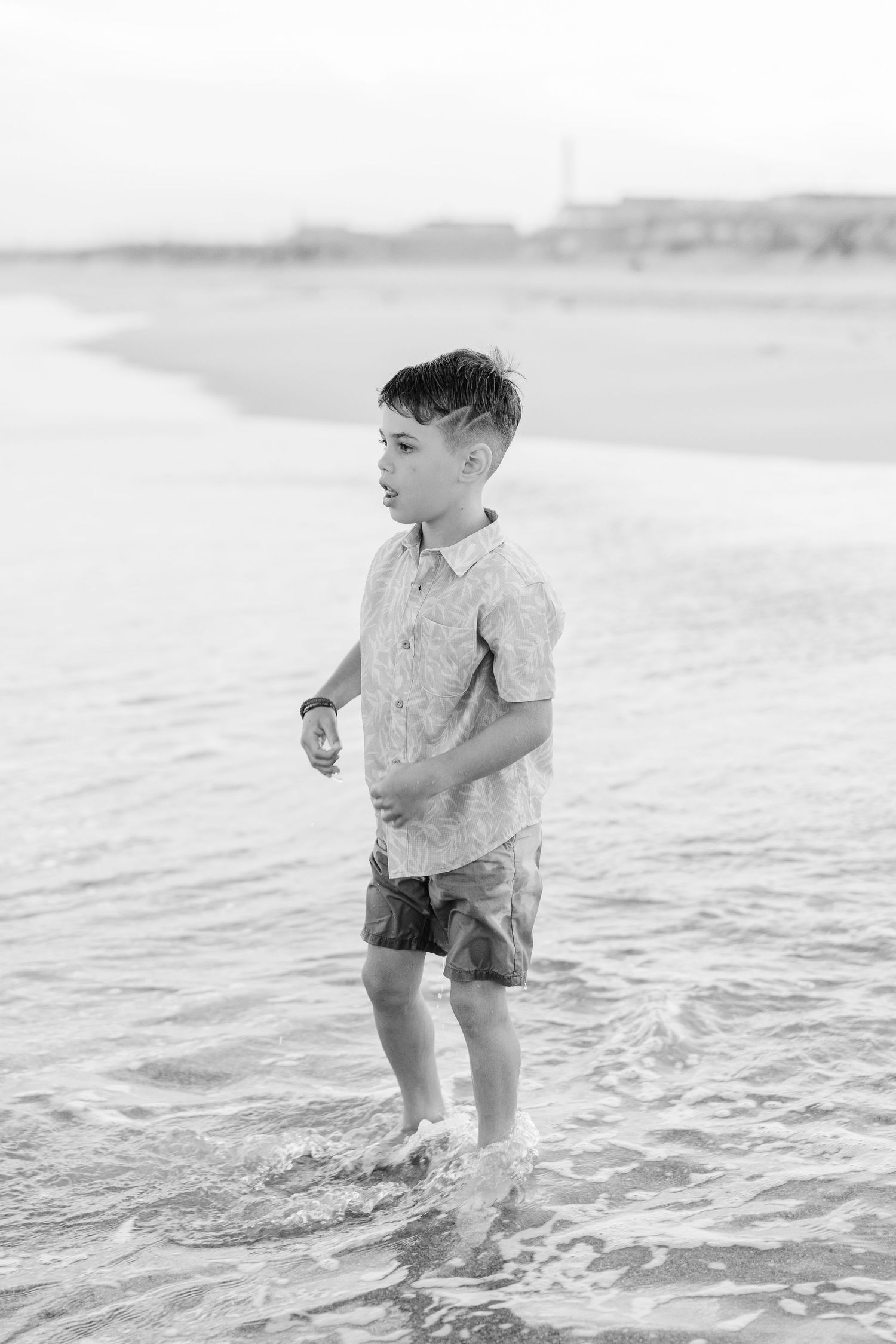 Young boy wading in ocean waves at beach in black and white photo.