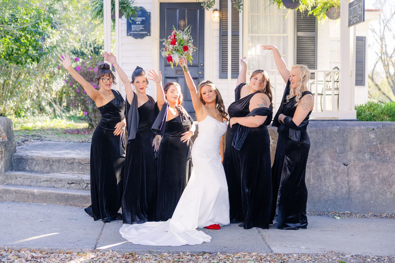 Wedding party poses playfully outside historic building with bridesmaids in black dresses.