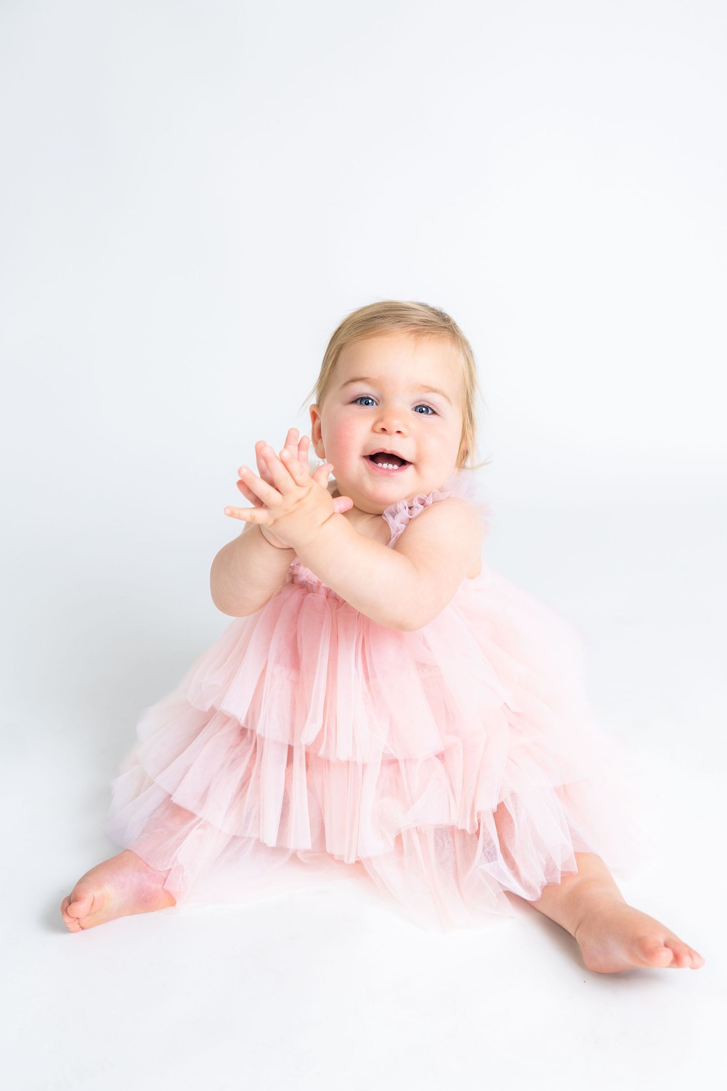 Baby in pink tulle dress playing on white background.