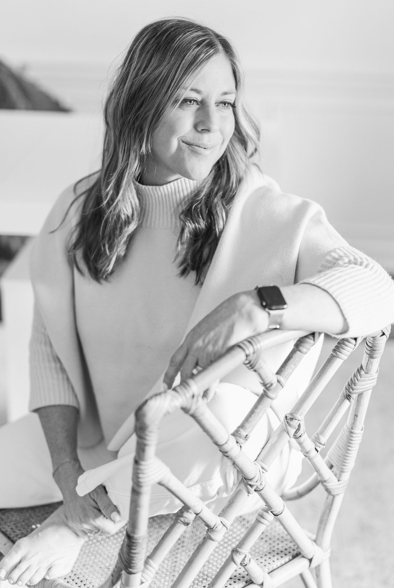 Black and white portrait of someone in cream turtleneck sweater sitting in woven chair.