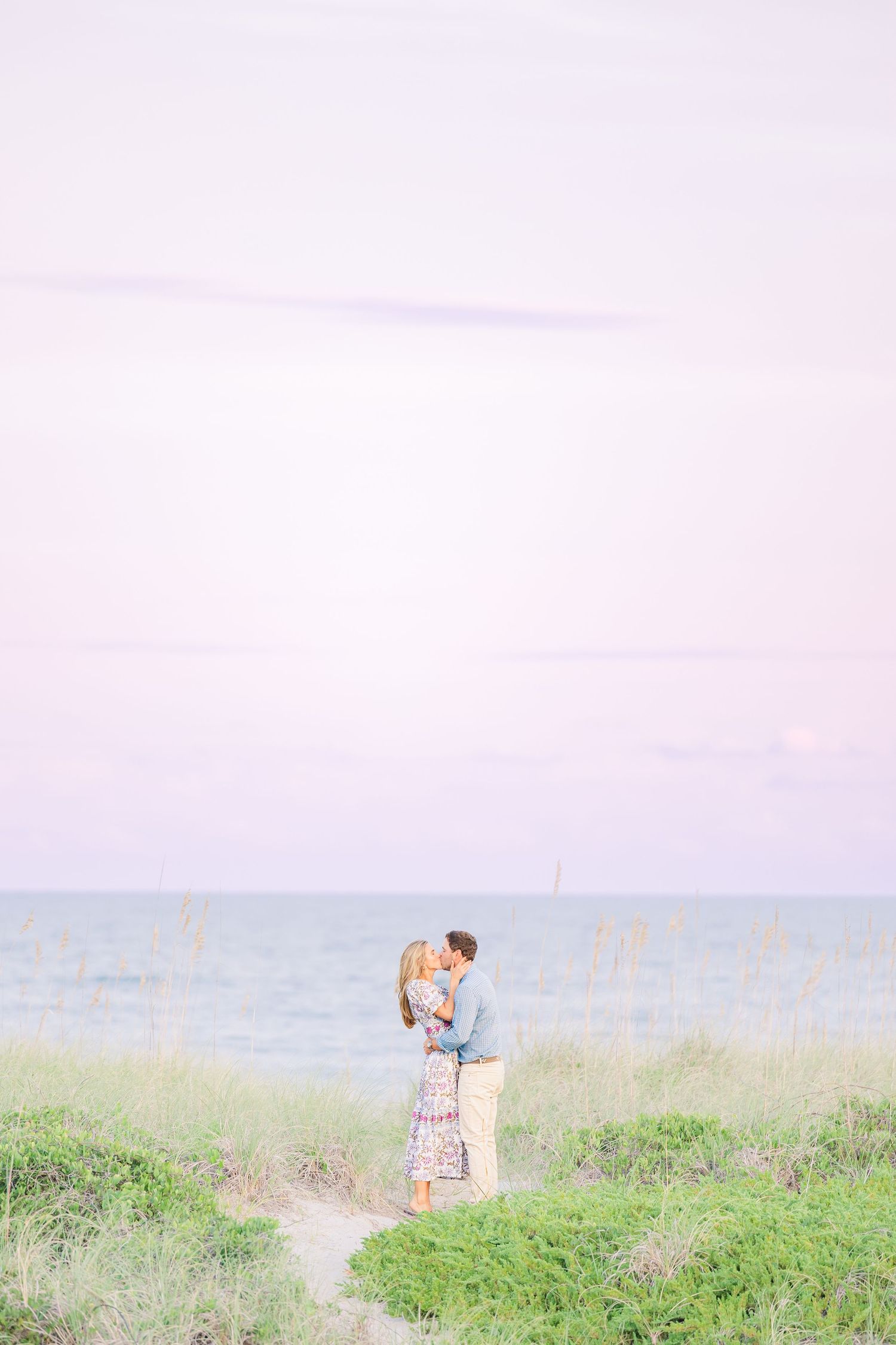 Couple standing together in a grassy coastal area with soft dreamy lighting.