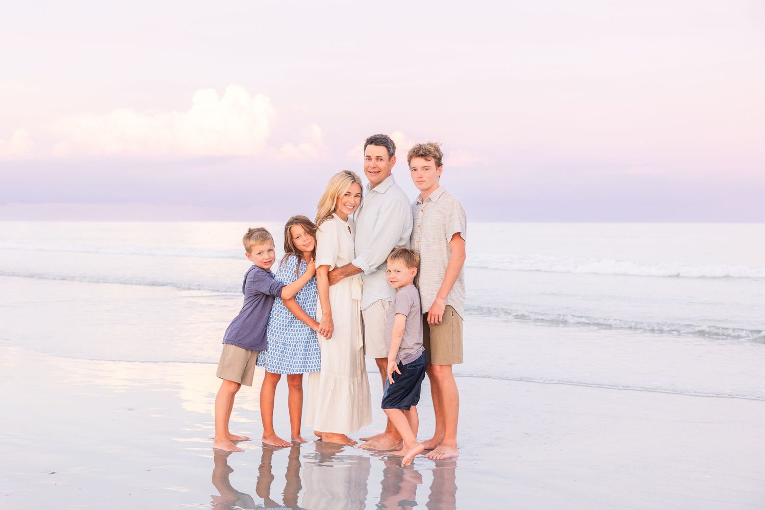 A family plays in the shallow ocean waves during a sunset photoshoot.