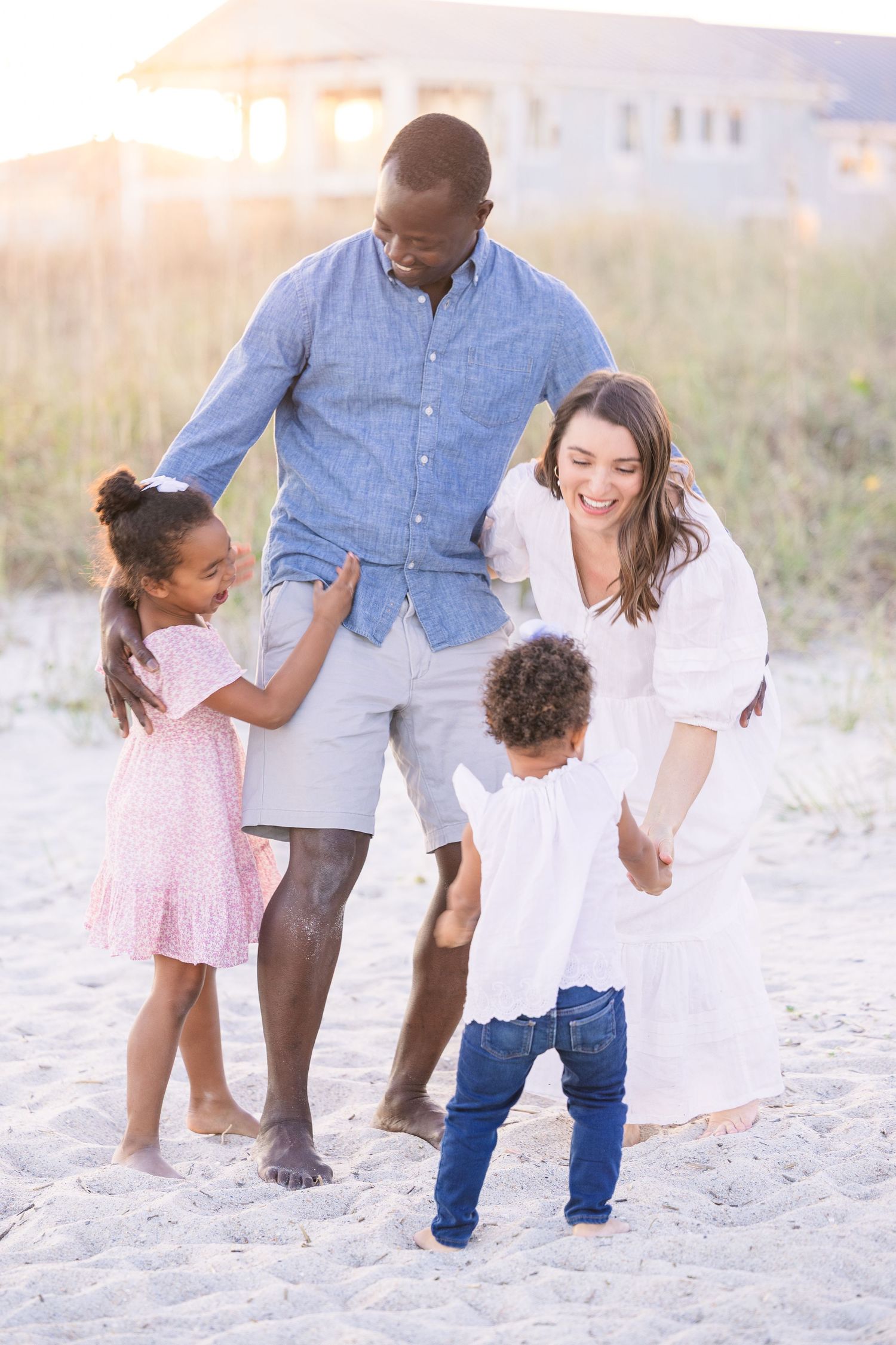 Family of four playing together on sandy beach with sunset glow.