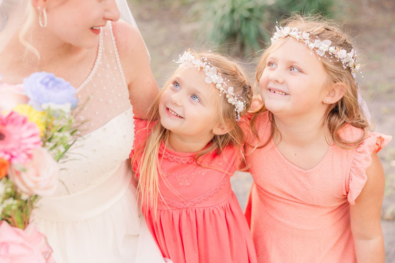 Bridesmaids share joyful laughter while wearing matching coral dresses at an outdoor celebration.