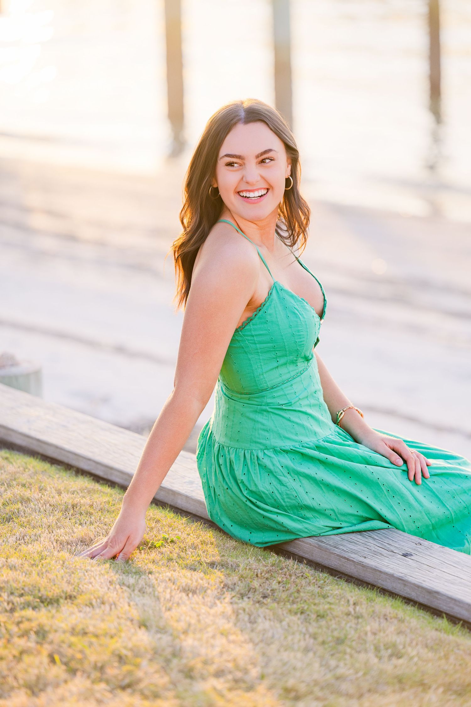 A vibrant green sundress stands out against wooden steps in a sunny outdoor portrait session.