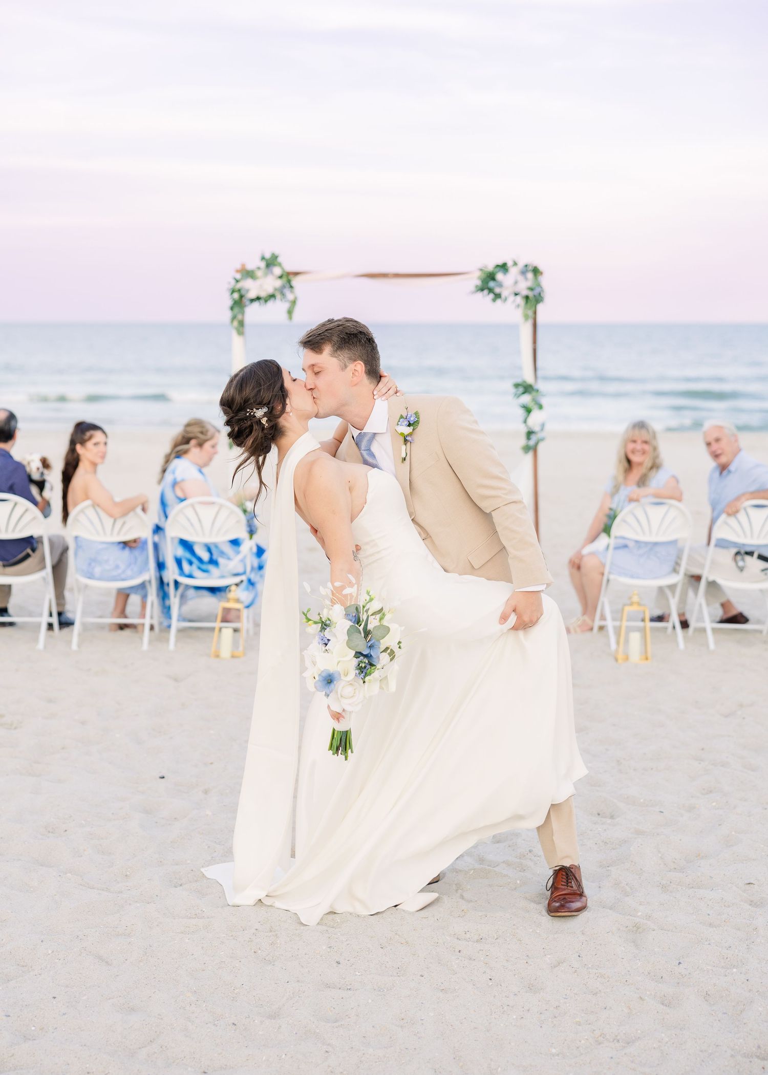 Bride and groom share a romantic kiss on the beach at sunset after their outdoor ceremony in Carolina Beach near Wilmington, NC.