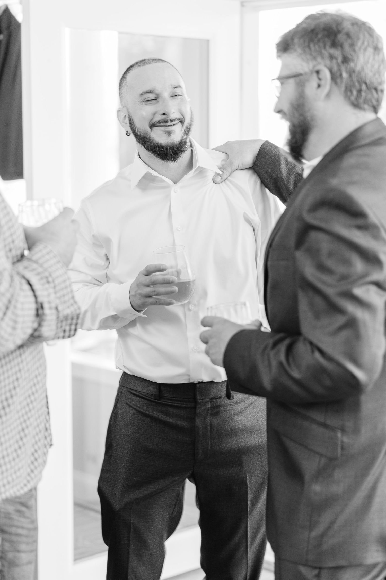 groom in formal attire interact and share drinks at an indoor gathering wedding groom bride lake Gaston photographer light airy