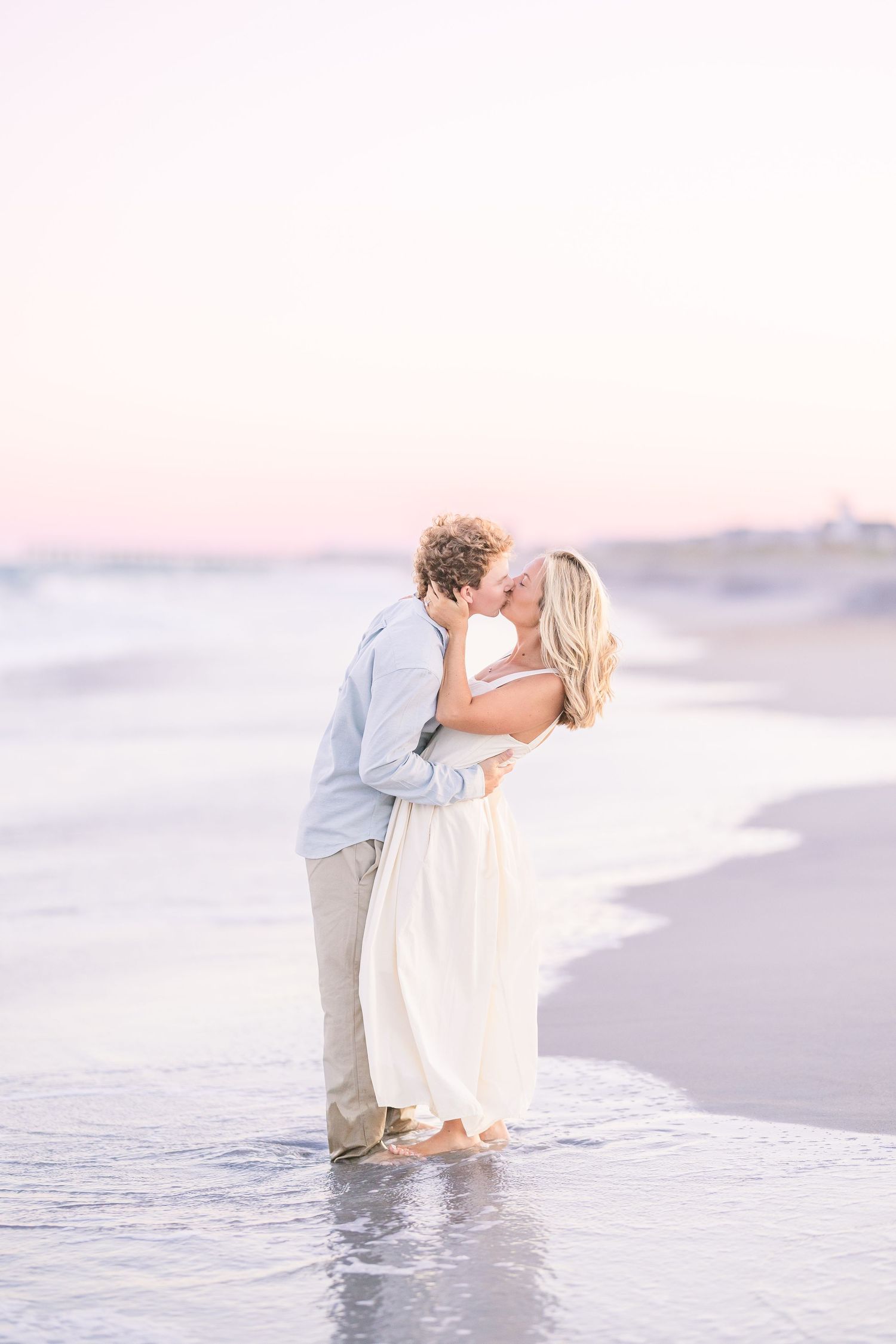 A romantic beach photoshoot with a couple dipping and embracing near the ocean waves at sunset.
