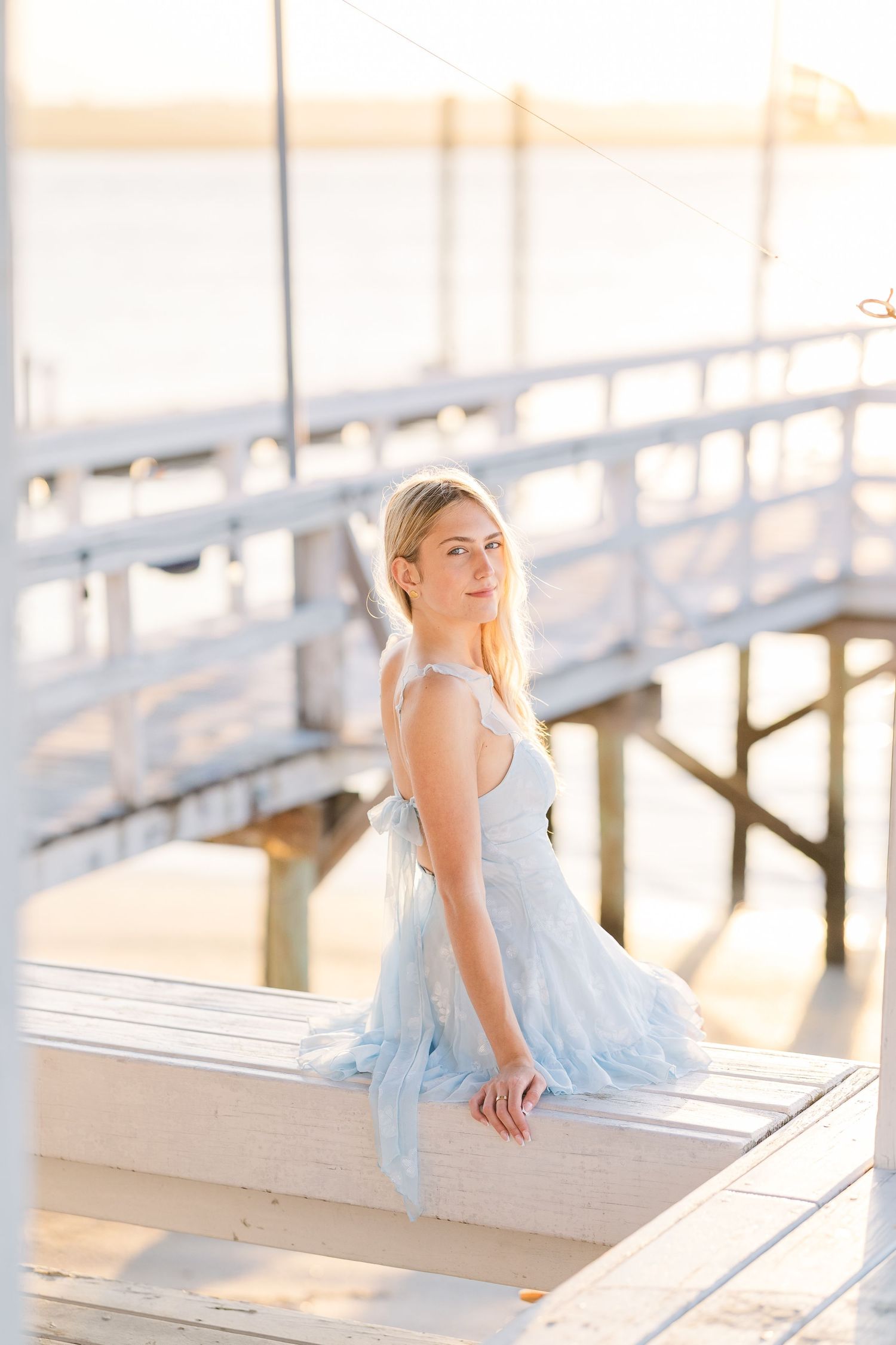 Ethereal seaside photo on white dock wearing flowing light blue dress.