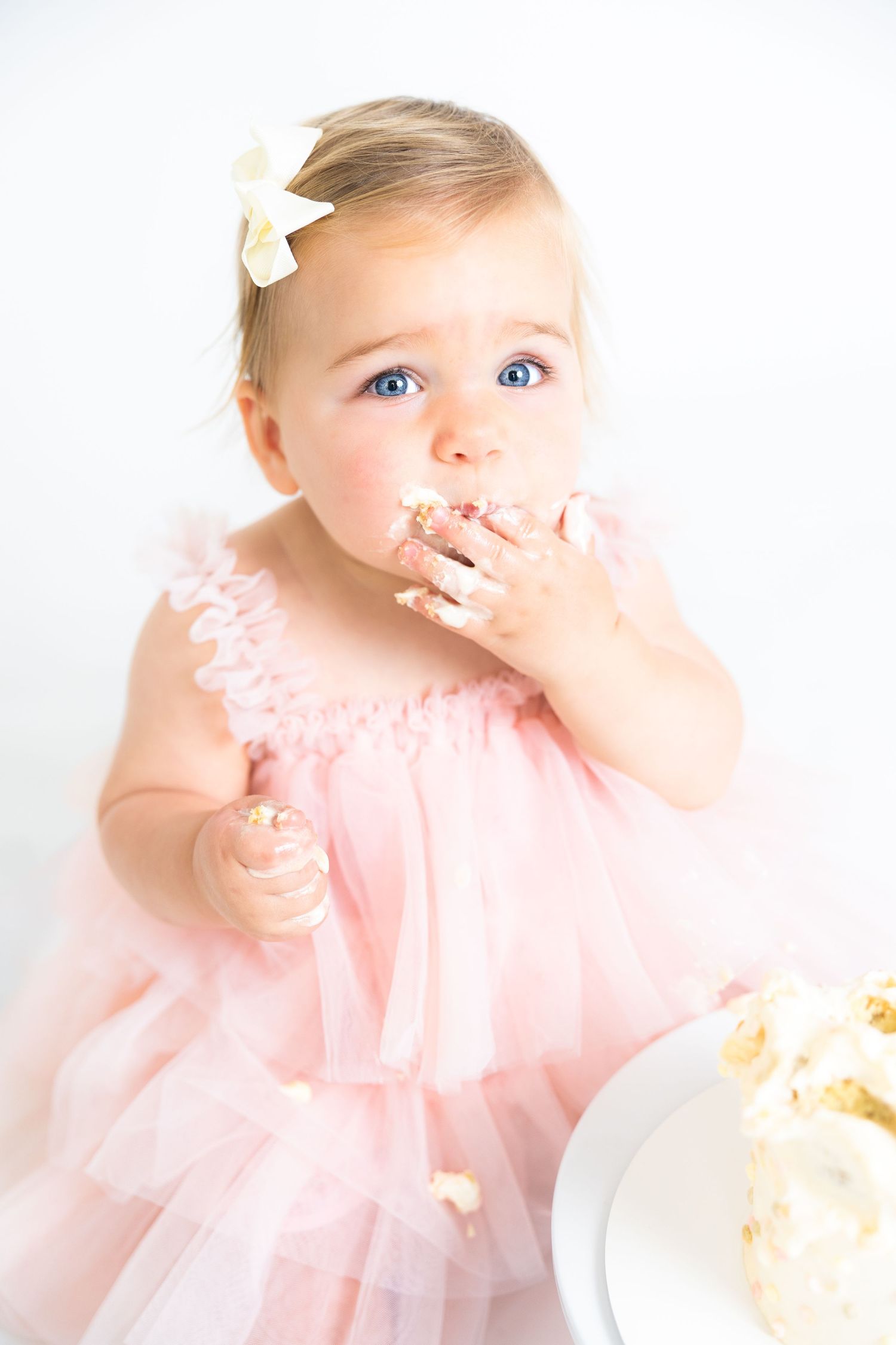 Baby in pink dress gets messy with cake during photo shoot.