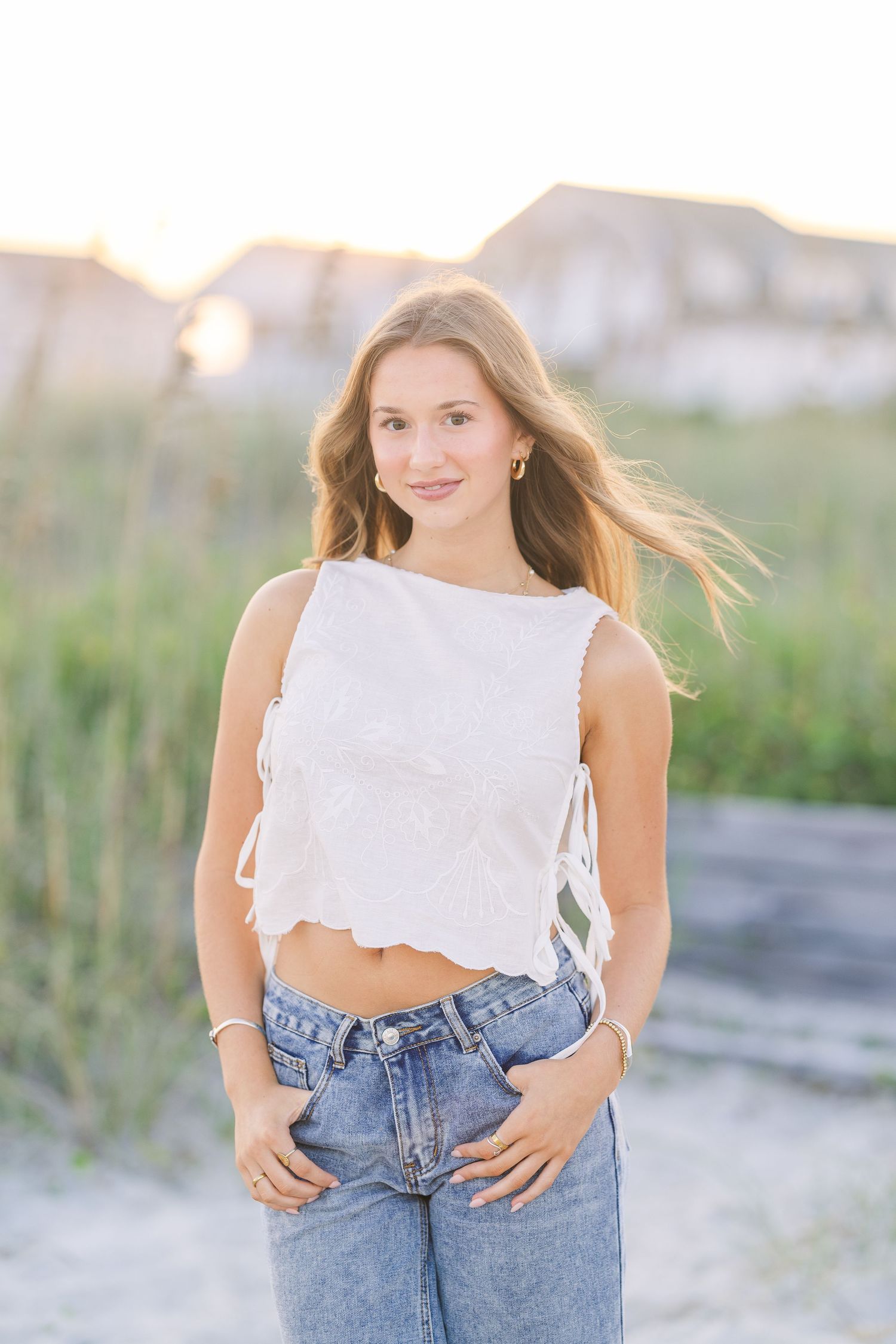 Summer fashion shoot on sandy beach with white crop top and high-waisted jeans.