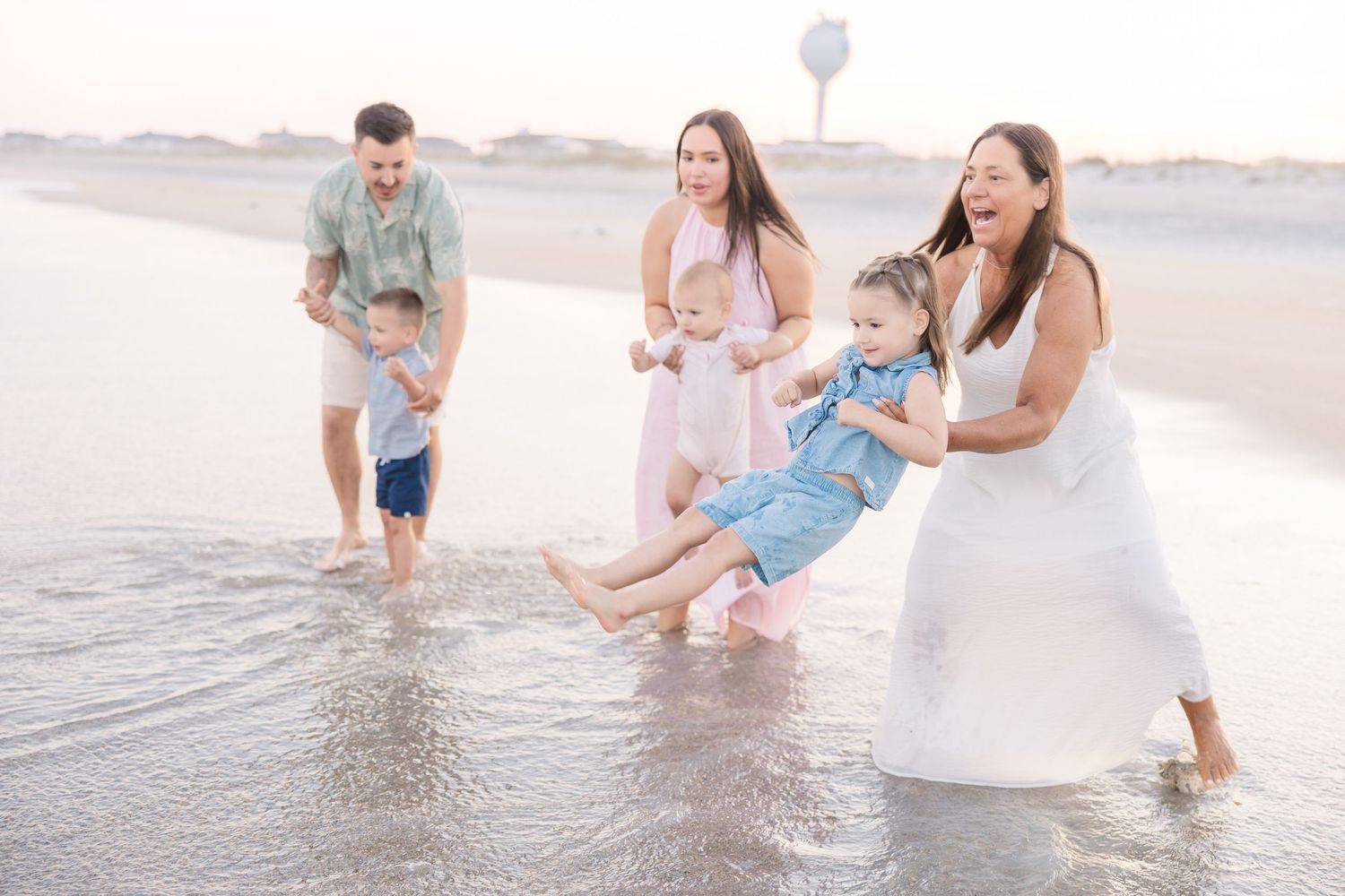 Family playing and laughing together in shallow ocean waves at the beach.
