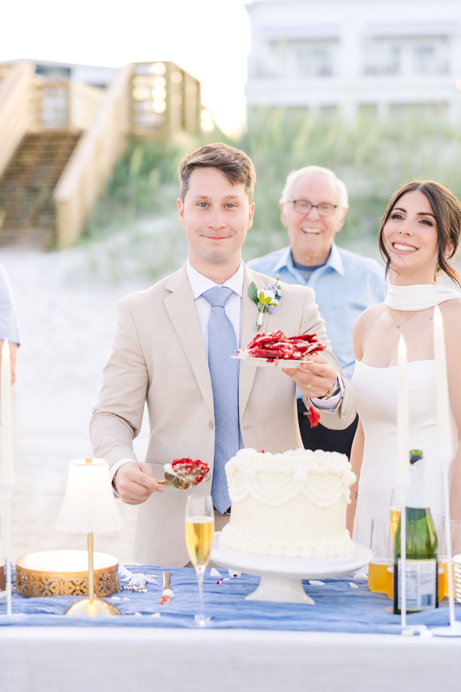 Groom in tan suit and bride cut wedding cake at outdoor beach reception with champagne in Carolina Beach near Wilmington, NC.