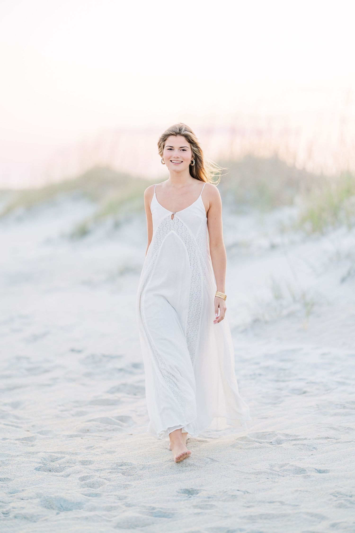 Dreamy beach photography with flowing white dress and gentle coastal breeze at dusk.