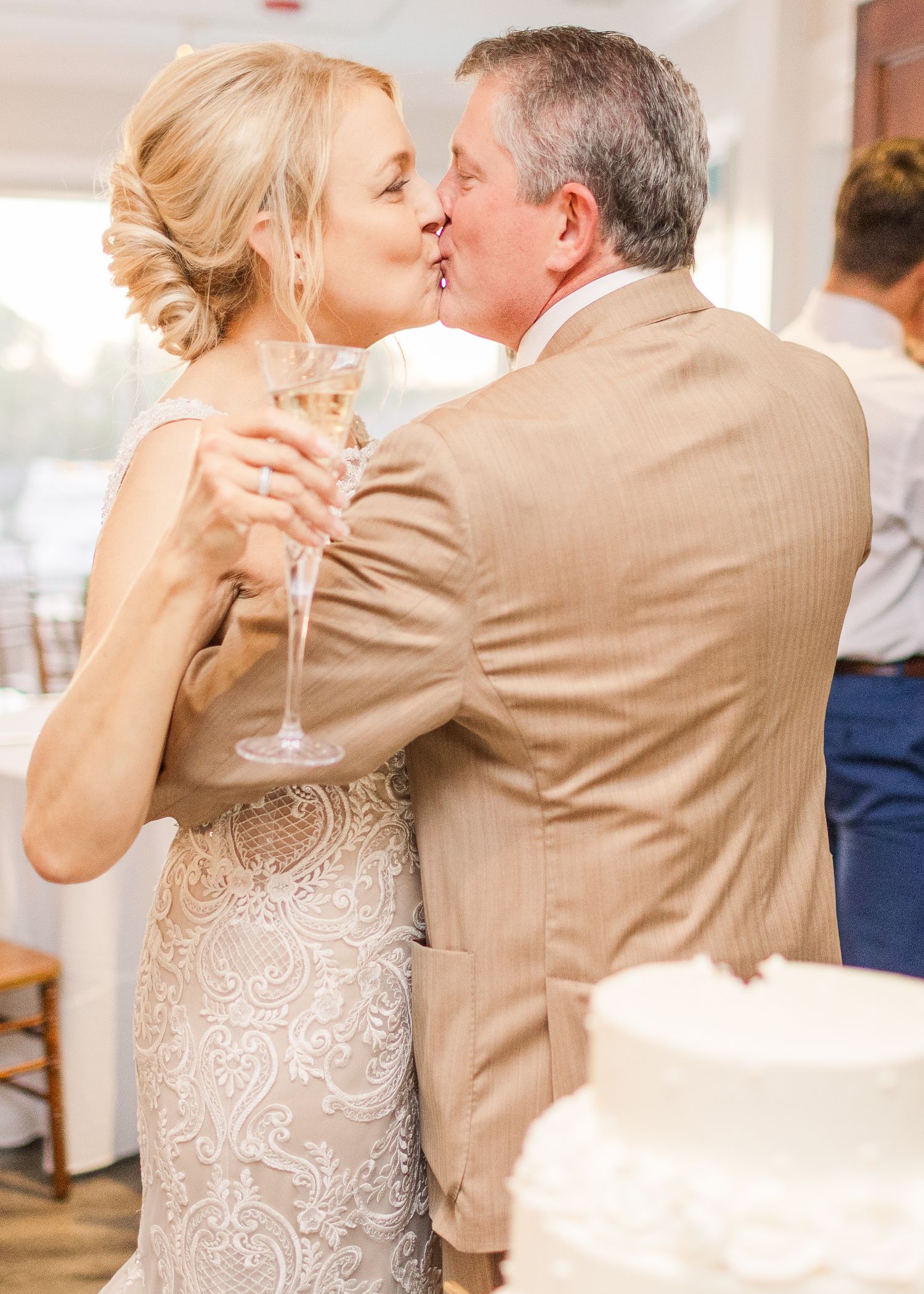 A romantic moment at a wedding reception as a couple shares a kiss while holding champagne glasses.