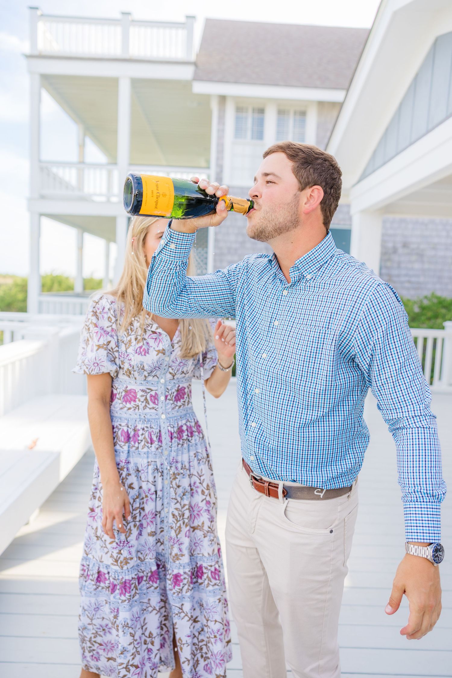 A couple drinks champagne together on a sunny white porch.