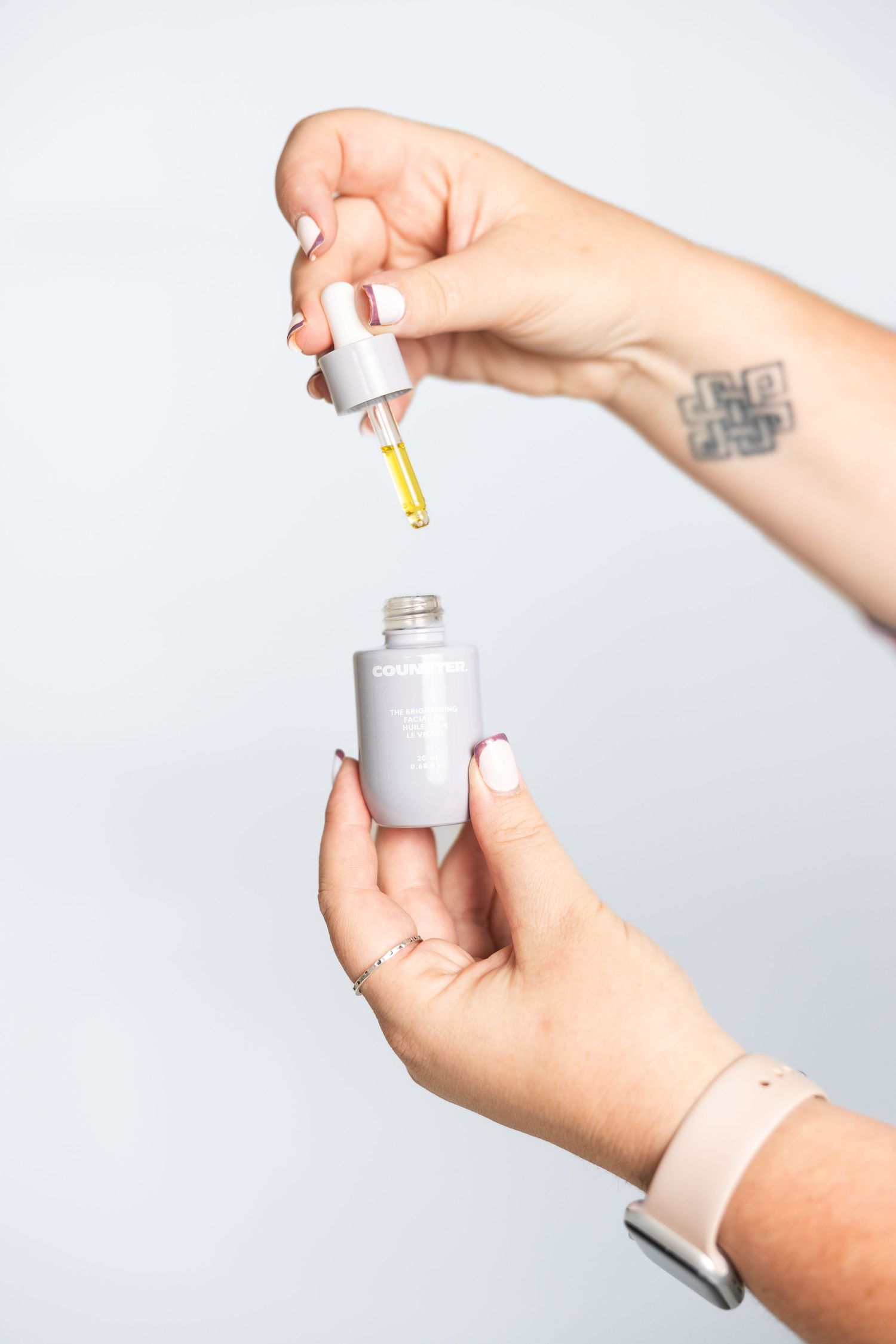 Hands demonstrating use of dropper bottle skincare product.