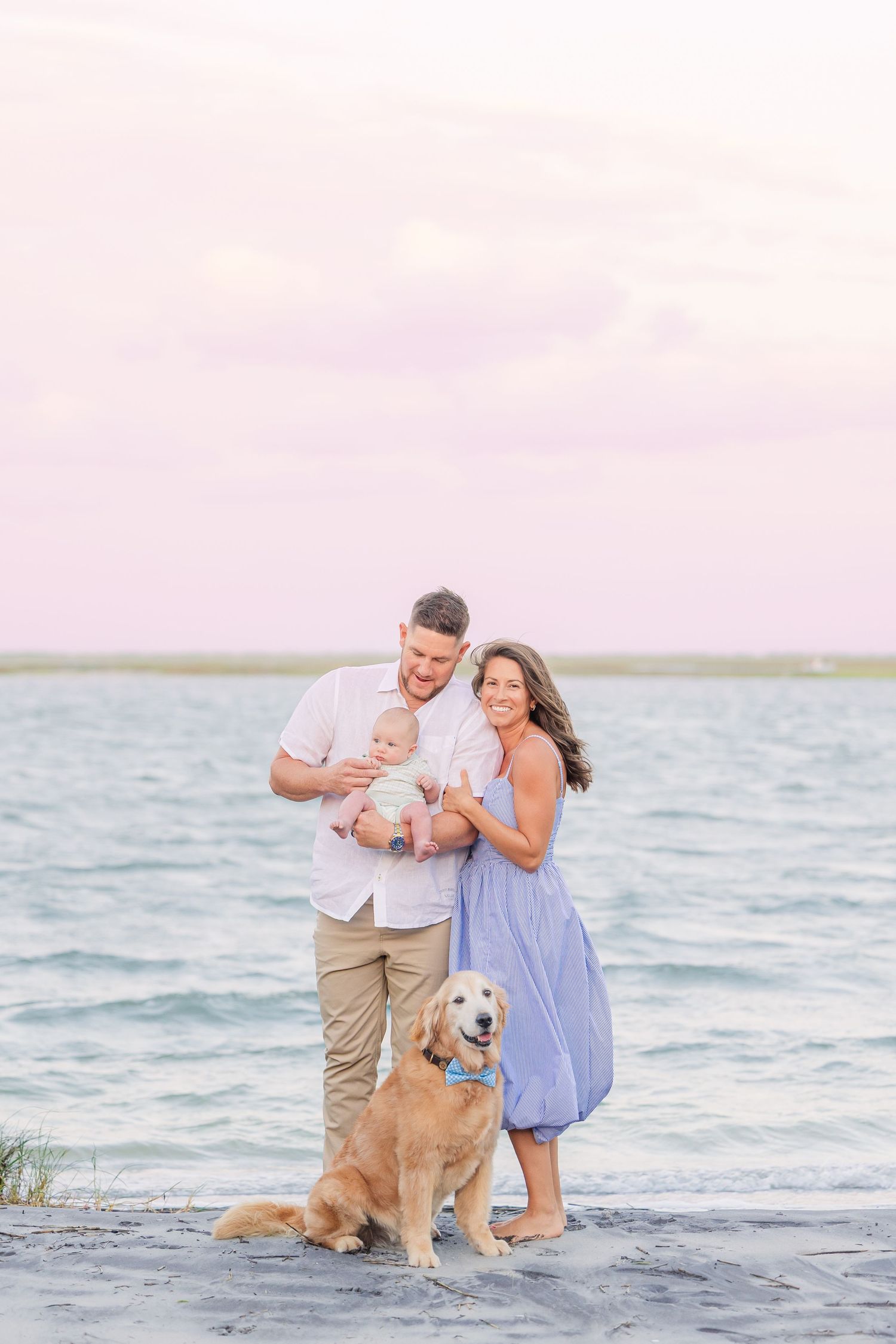 Family with golden retriever playing together at the water's edge during golden hour.