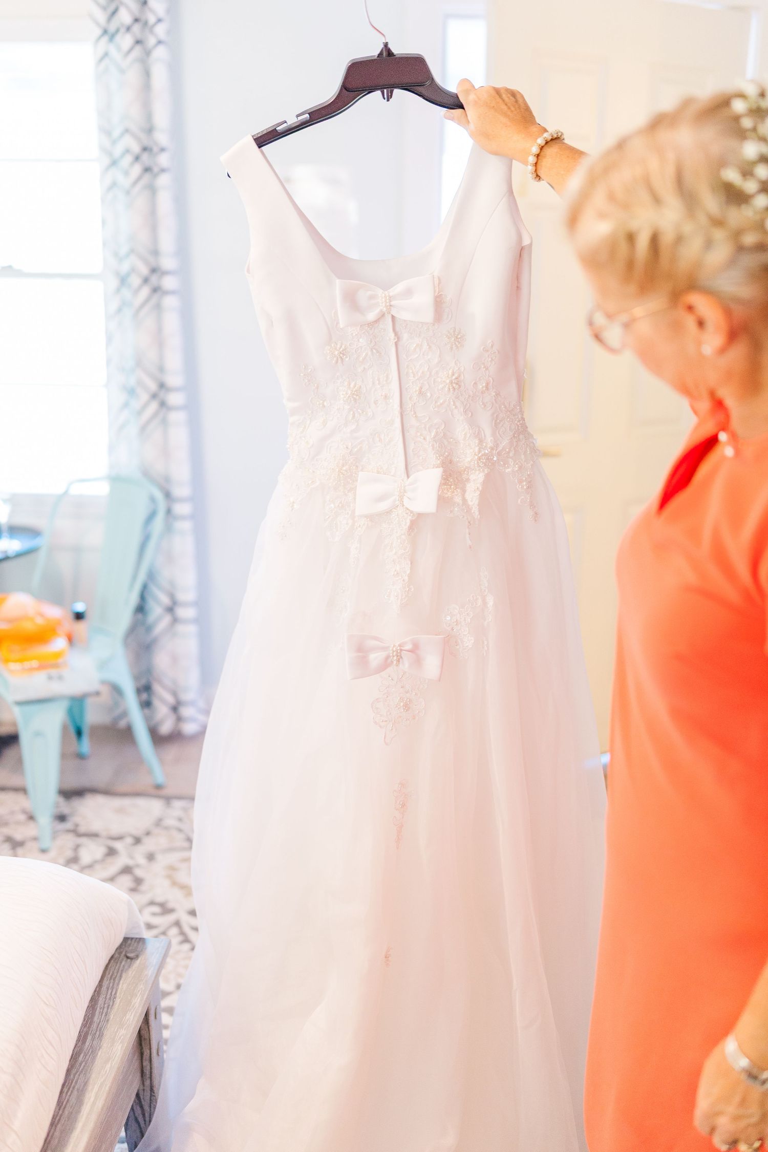 White wedding dress displayed on hanger with delicate lace details in bright room southport elopement wedding bride groom light and airy