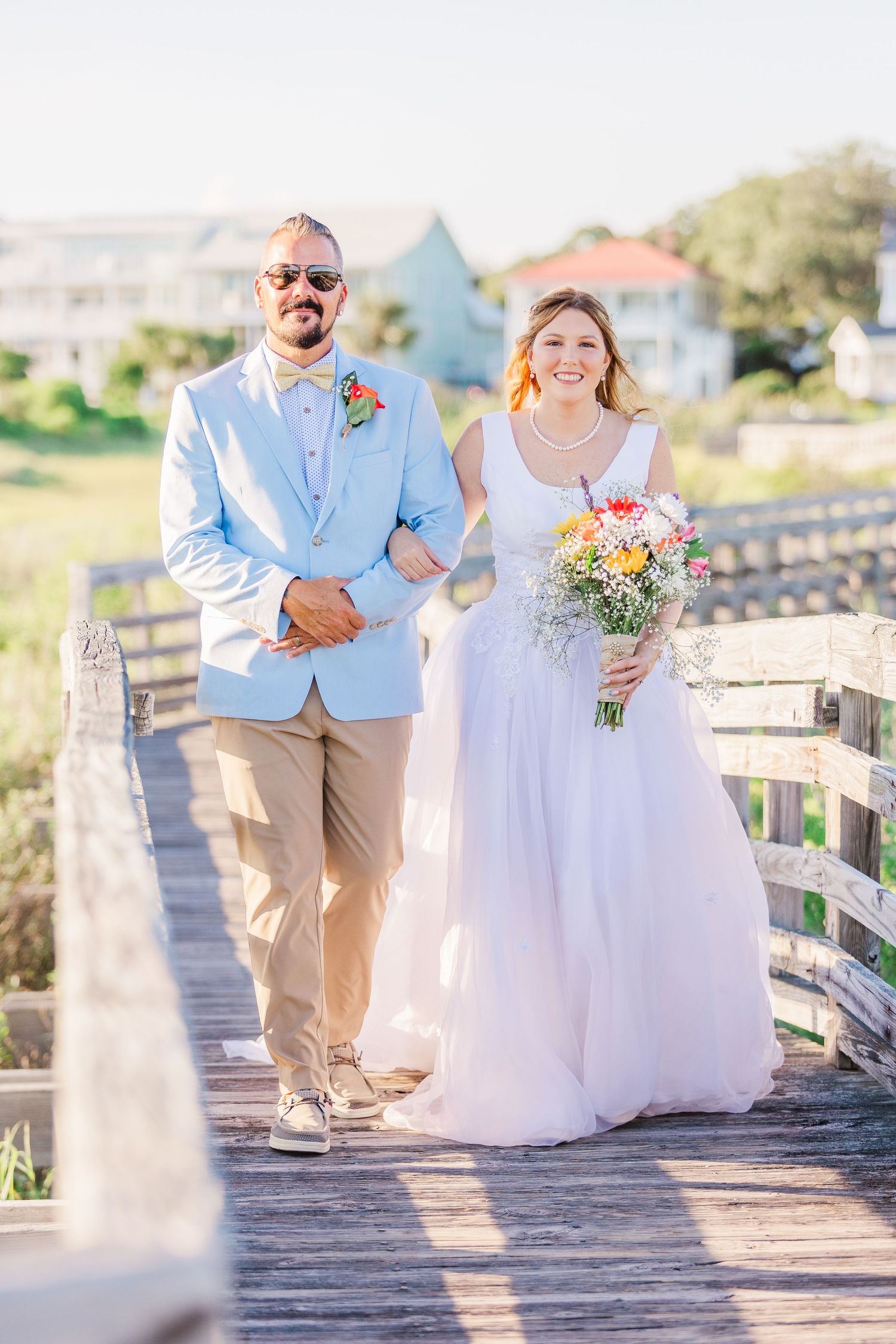 Wedding party walks along a coastal boardwalk carrying bouquets of flowers southport elopement wedding bride groom light and airy classic