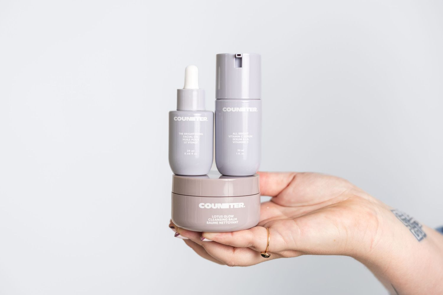 Hands holding white skincare product containers against light background.