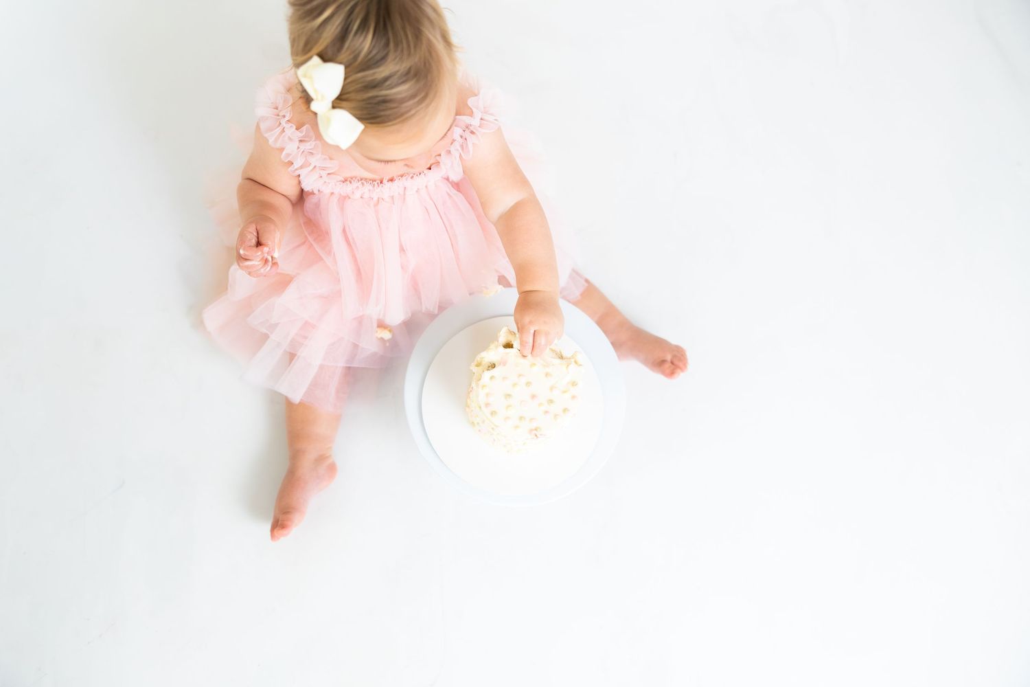 Small child in pink dress explores white cake during photo session.
