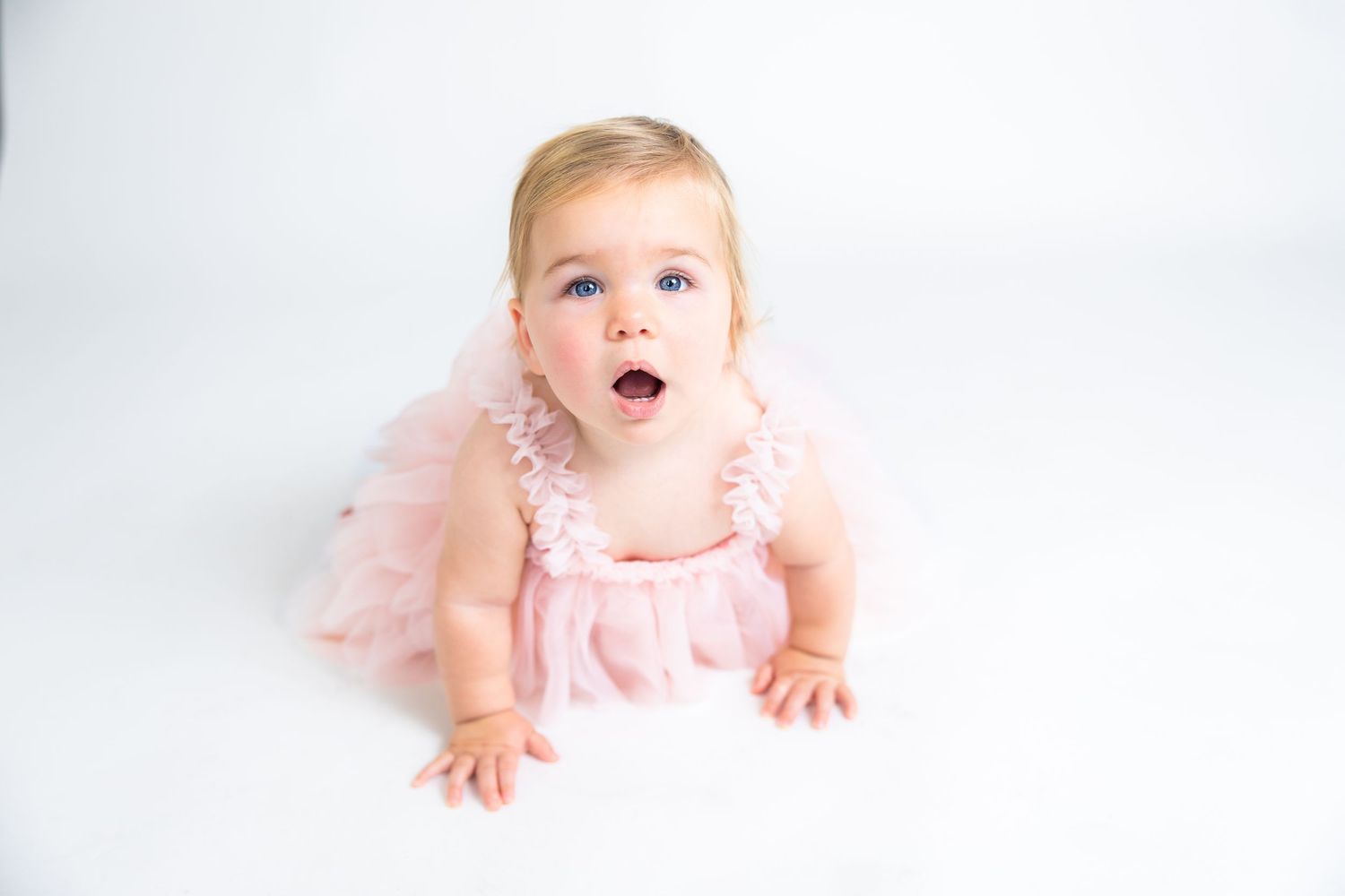 Baby in pink tulle dress lying on white background with joyful expression.