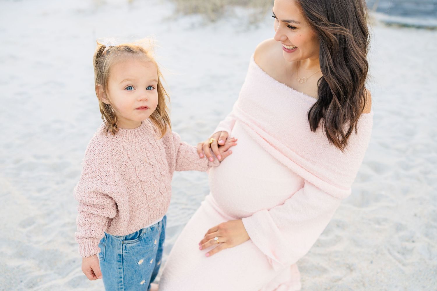 Mother and child share tender moment on beach in coordinating pink outfits.