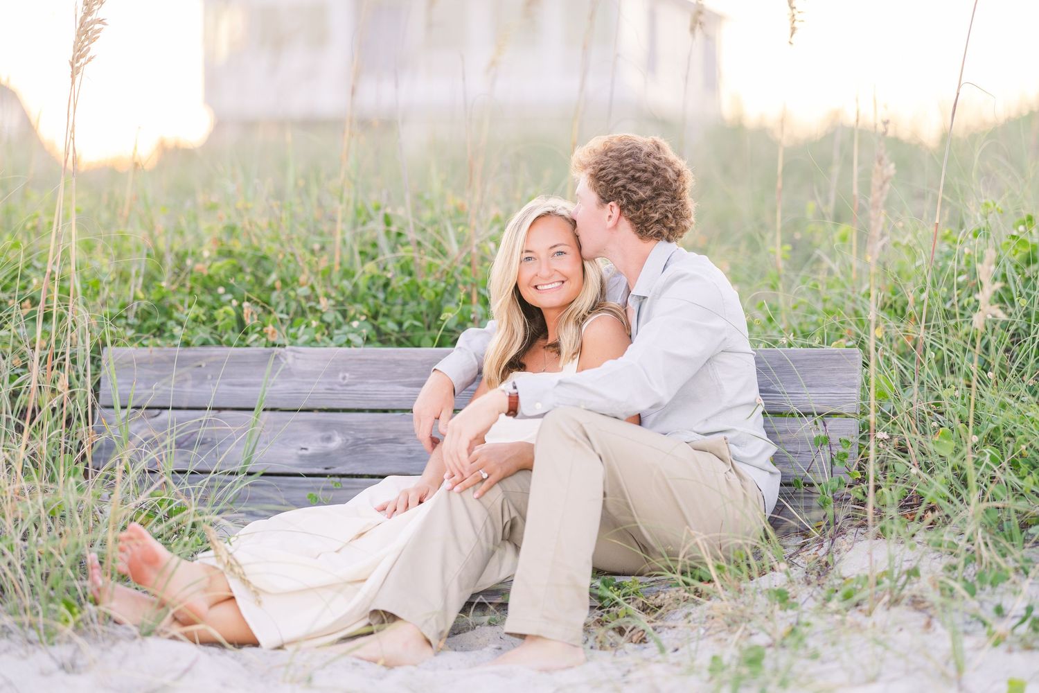 Romantic couple's portrait session on a wooden walkway surrounded by coastal grass at sunset.