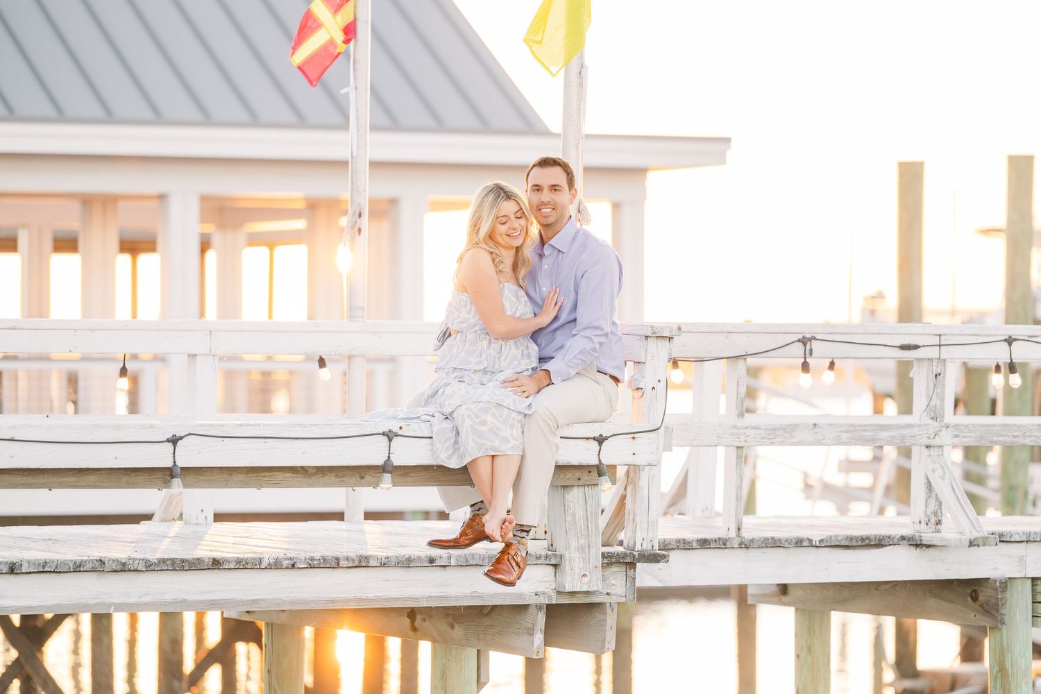 Golden hour portrait of couple sitting together on wooden dock by water.