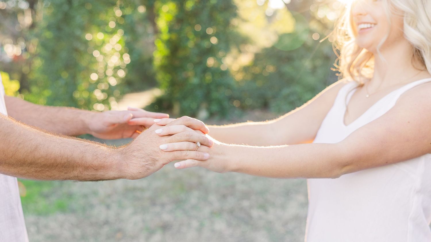 A couple dancing and twirling together in white outfits against a sunlit natural backdrop.