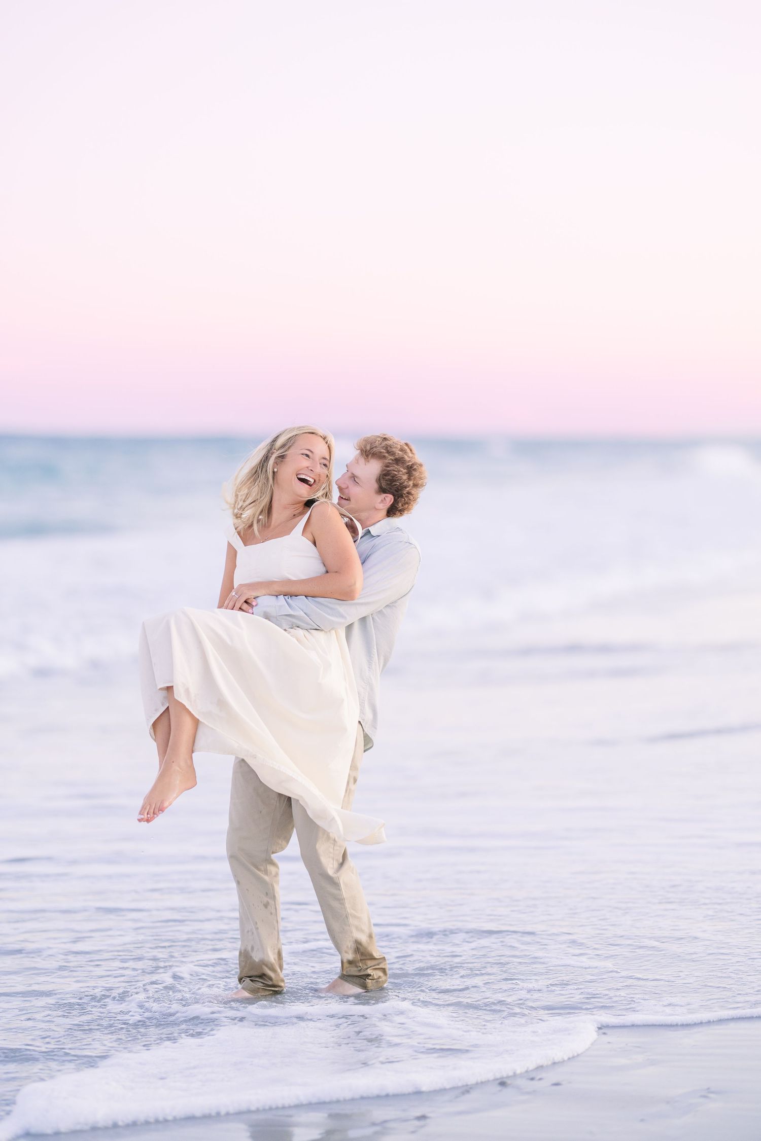 Playful beach scene with couple splashing in shallow ocean water at sunset.