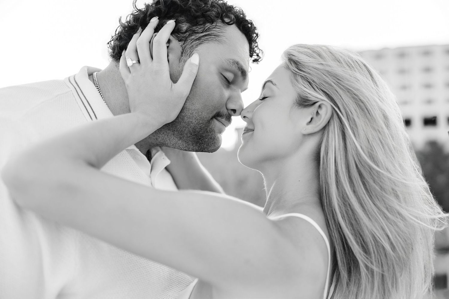 Black and white romantic photo of couple almost kissing, woman with long blonde hair embracing man.