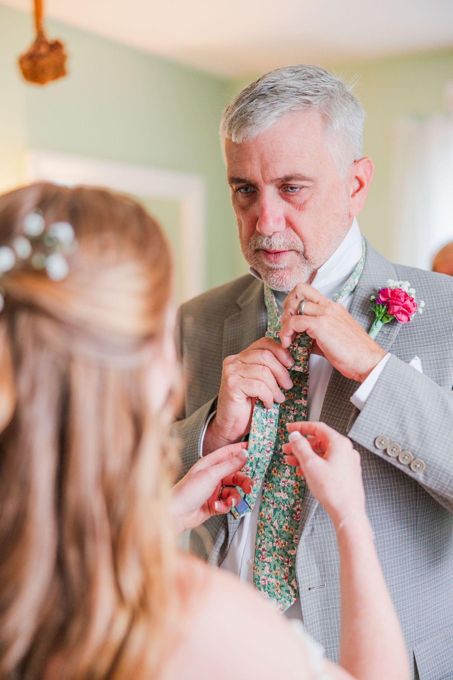 A touching moment as someone helps adjust a floral tie during wedding preparations in a backyard wedding in wilmington, nc